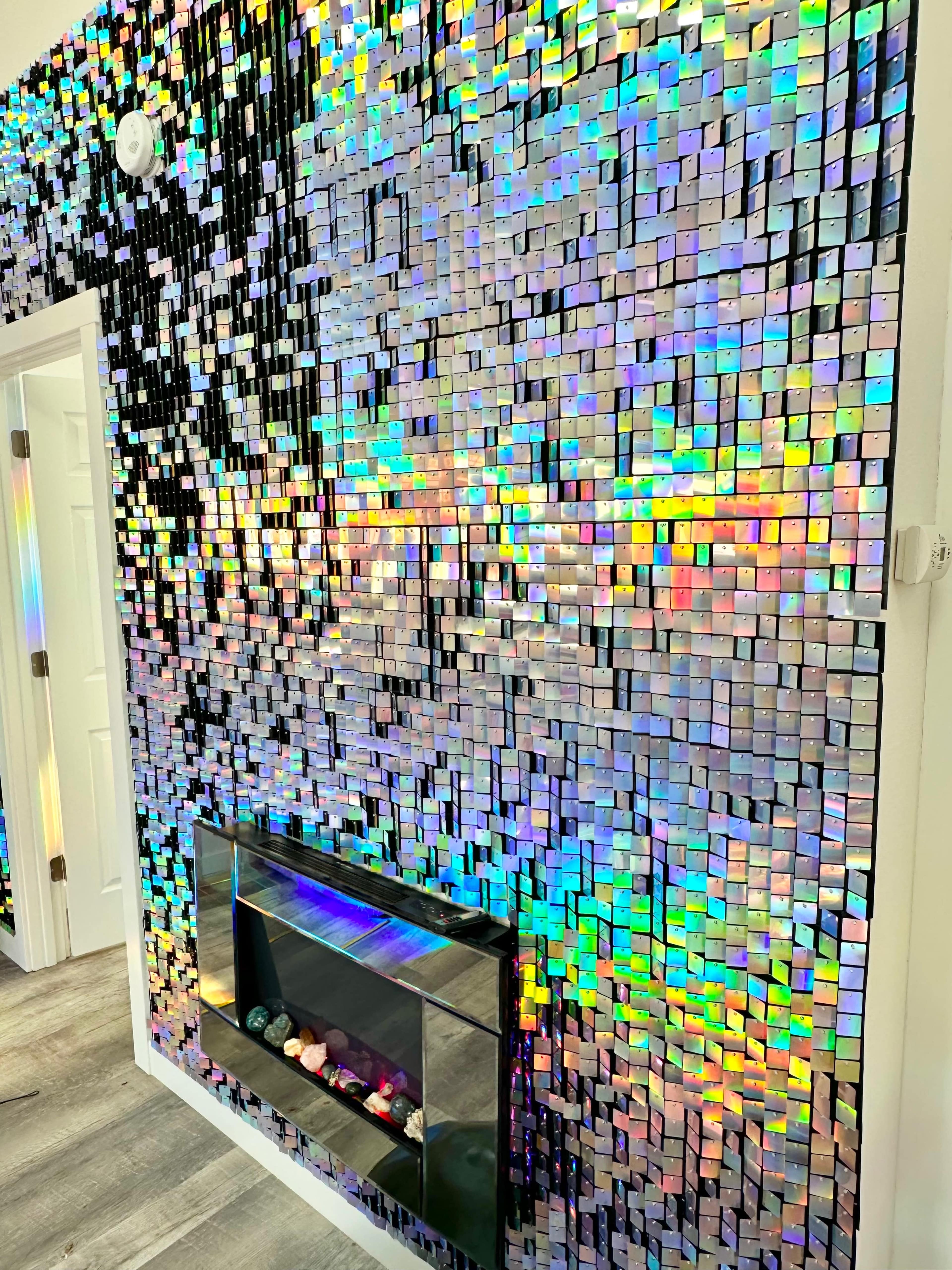 A wall covered in small, reflective, square tiles that create a colorful, shimmering effect alongside a modern electric fireplace.