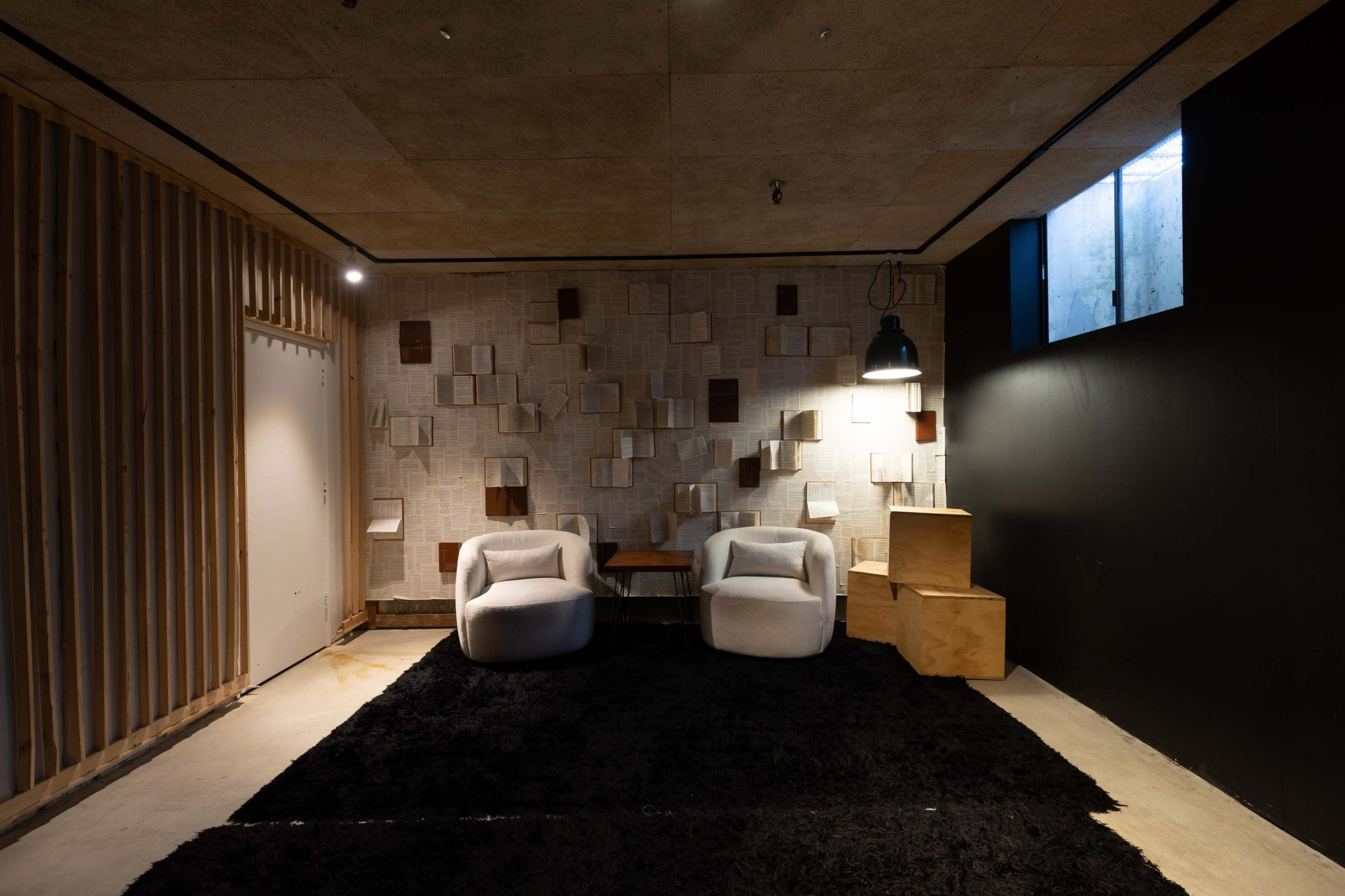 The image shows a contemporary interior space featuring two white chairs, a wooden table, and a textured wall with various wooden panels, all set against a dark carpet.