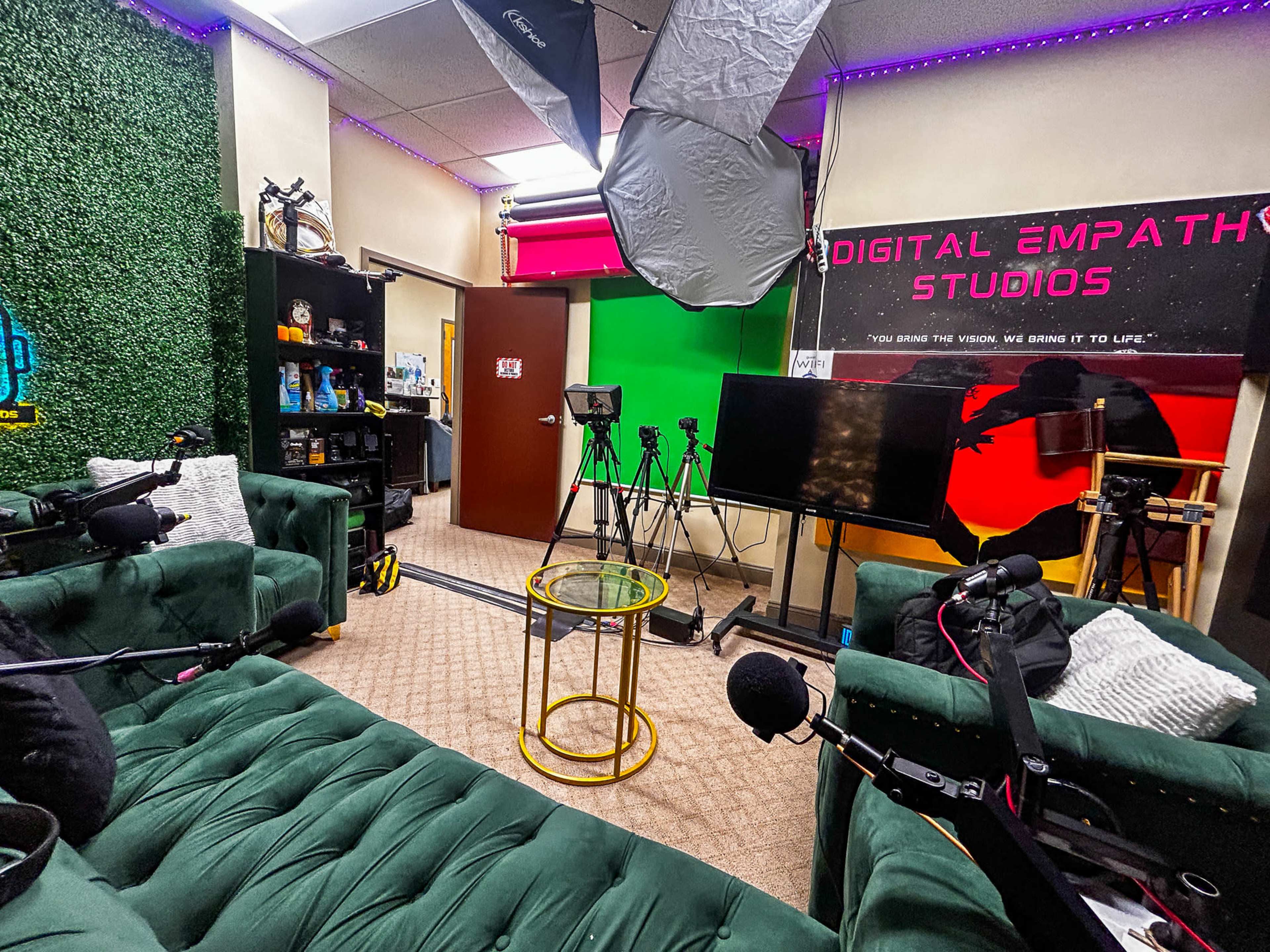 The image shows a studio equipped with green and black walls, a small round table, microphones, and multiple cameras set up for video production.