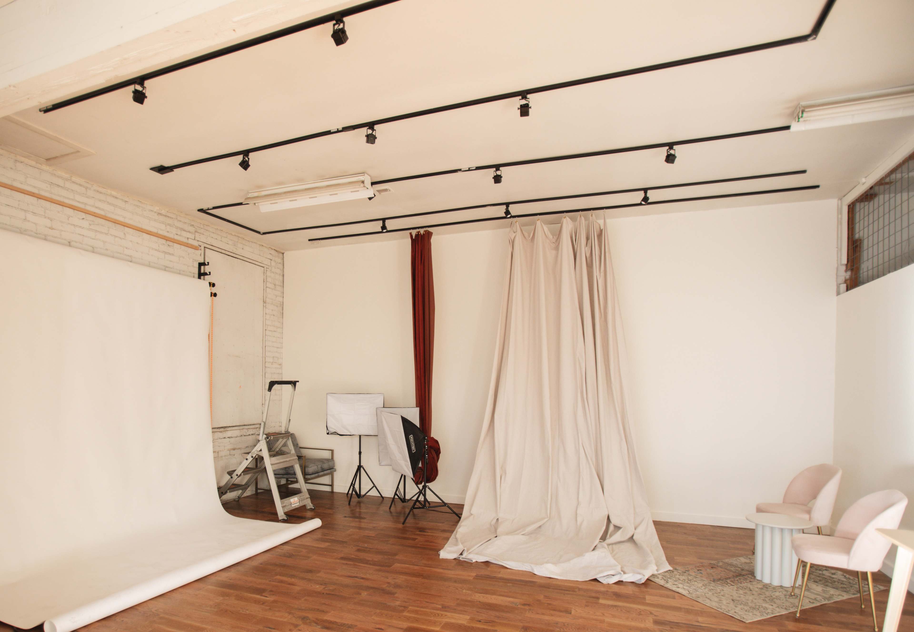 The image shows a photography studio with a backdrop, lighting equipment, and neutral-colored drapes.