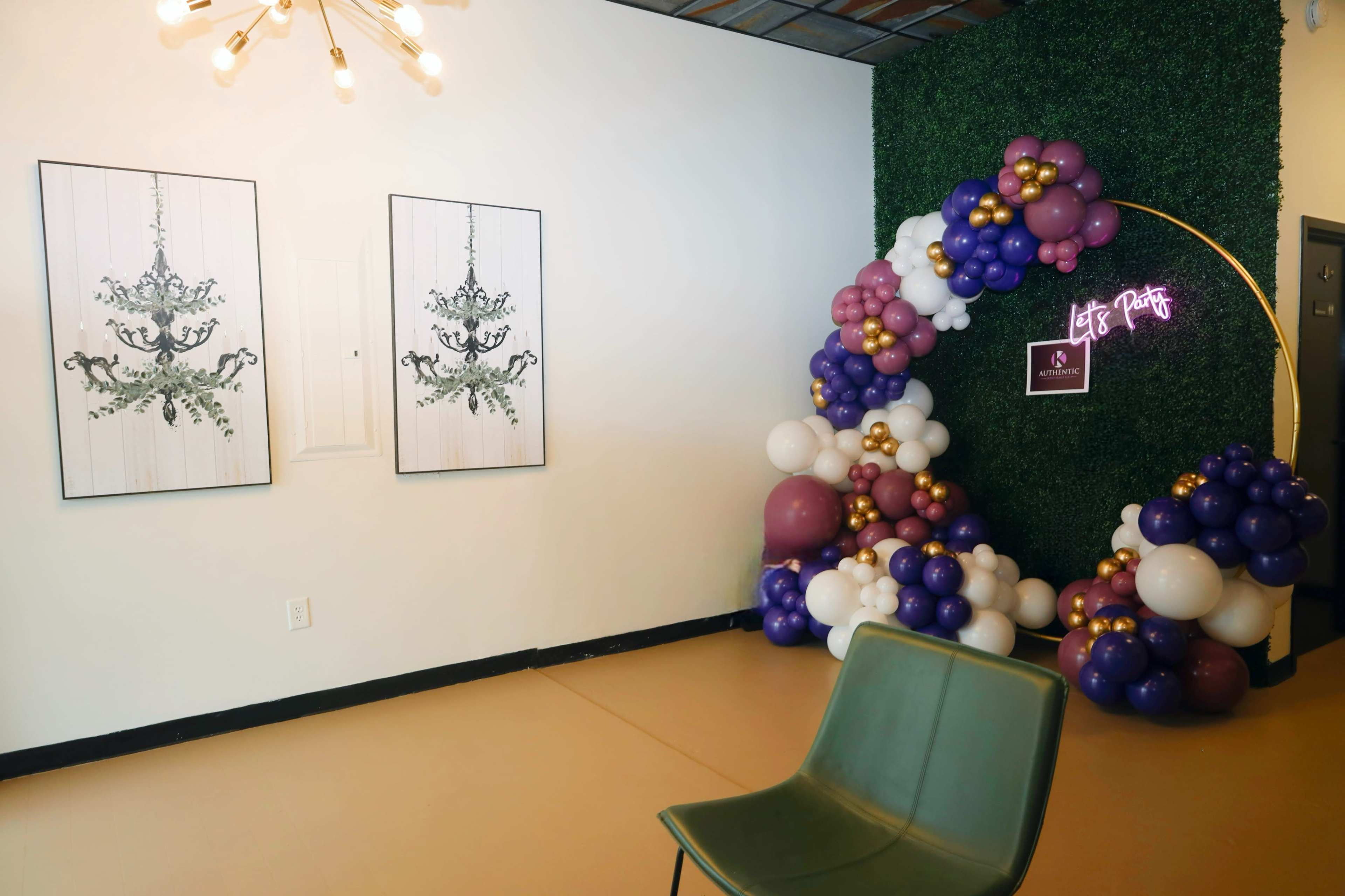 The scene features a modern interior with two framed art pieces resembling chandeliers on the left and a colorful balloon arch with a neon sign reading "Let's Party" on the right.
