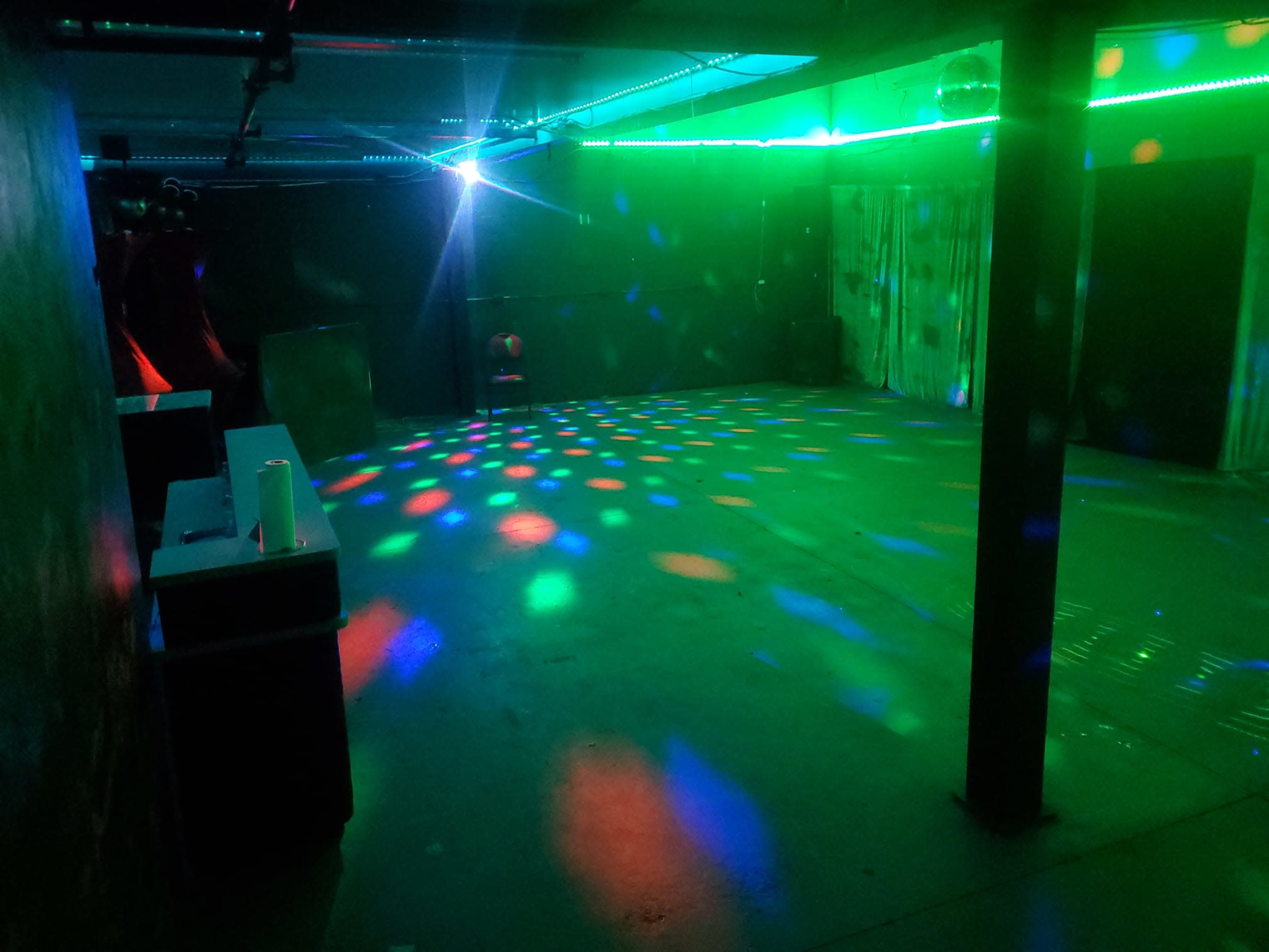 The image shows an empty room with a colorful light display creating patterns on the floor, and a single chair positioned in the space.