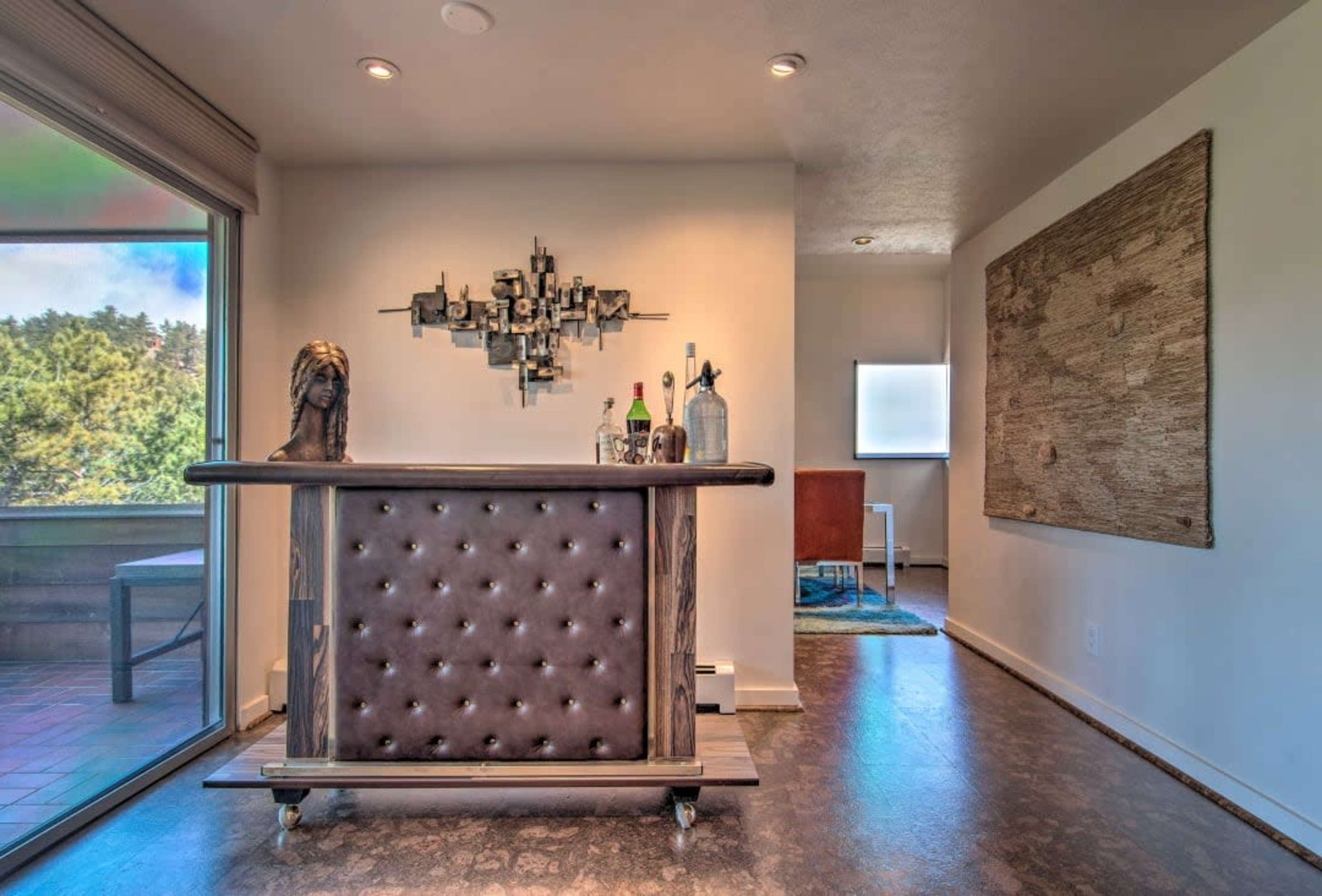 A modern home bar area with a tufted, dark leather counter and decor featuring a wall sculpture and bottles on the bar.