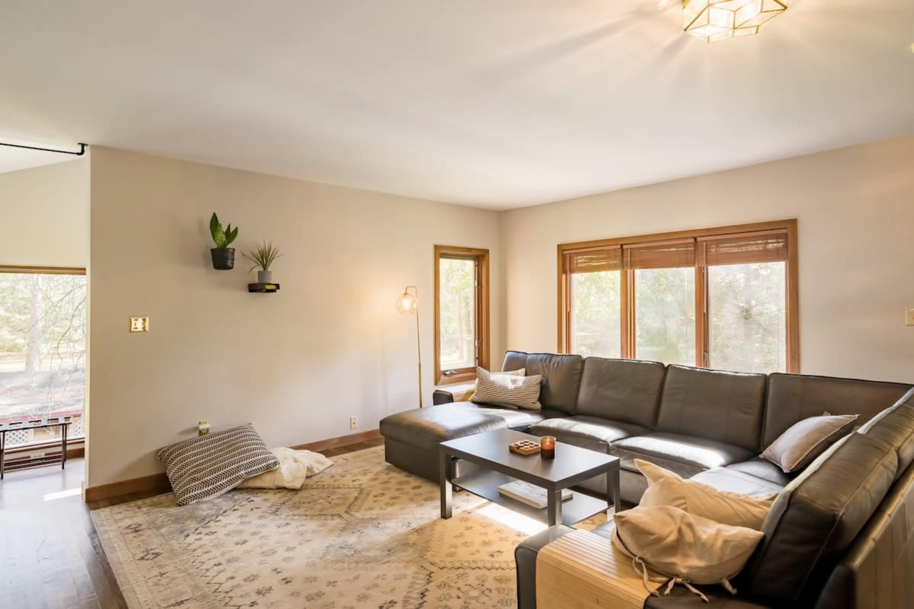 A modern living room with a large sectional couch, a coffee table, and windows providing natural light.