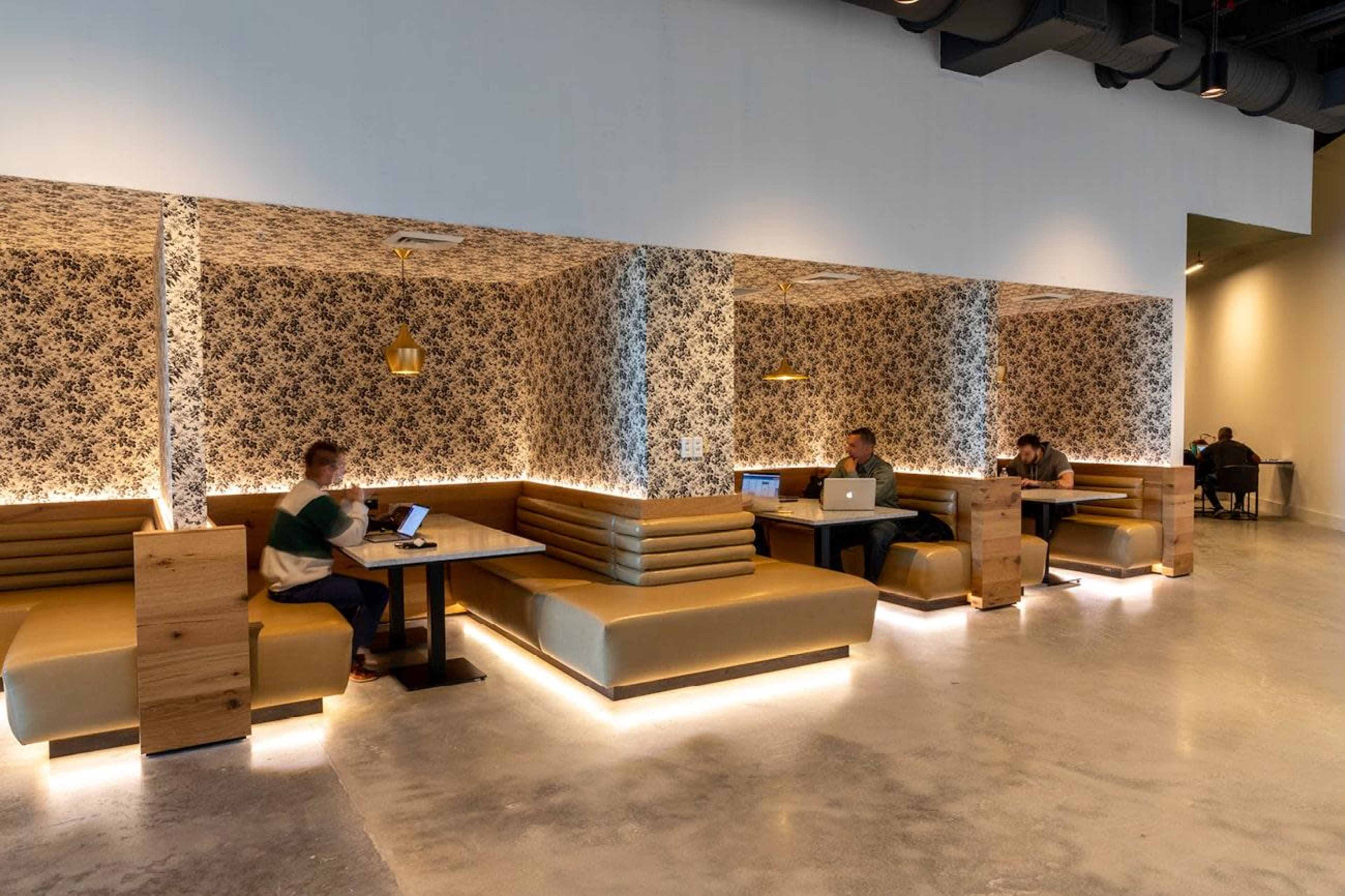 The image shows a modern café interior with booth seating, patterned wallpaper, and people working on laptops.