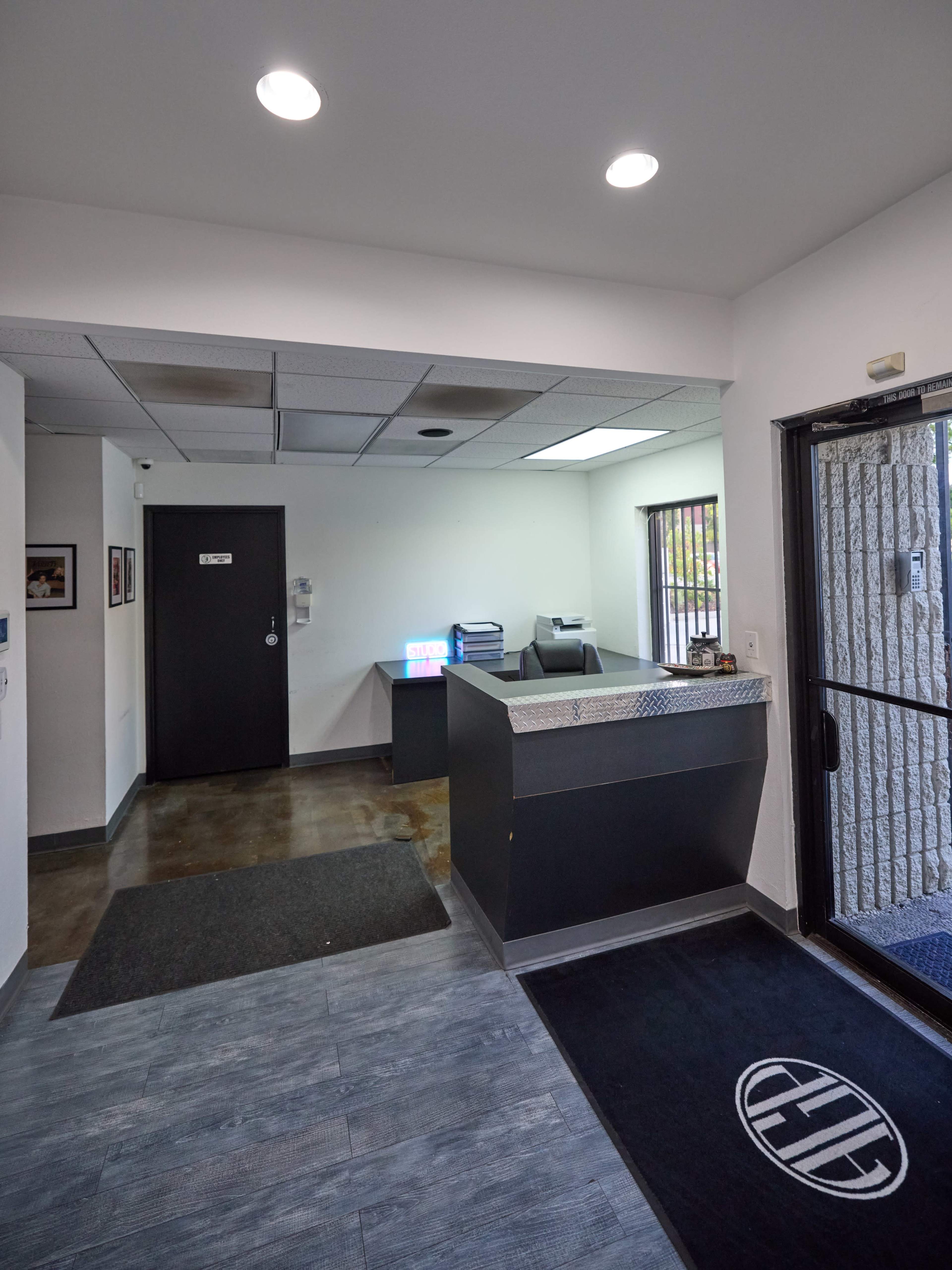 A modern office reception area with a front desk, door, and a view into another room with a printer.