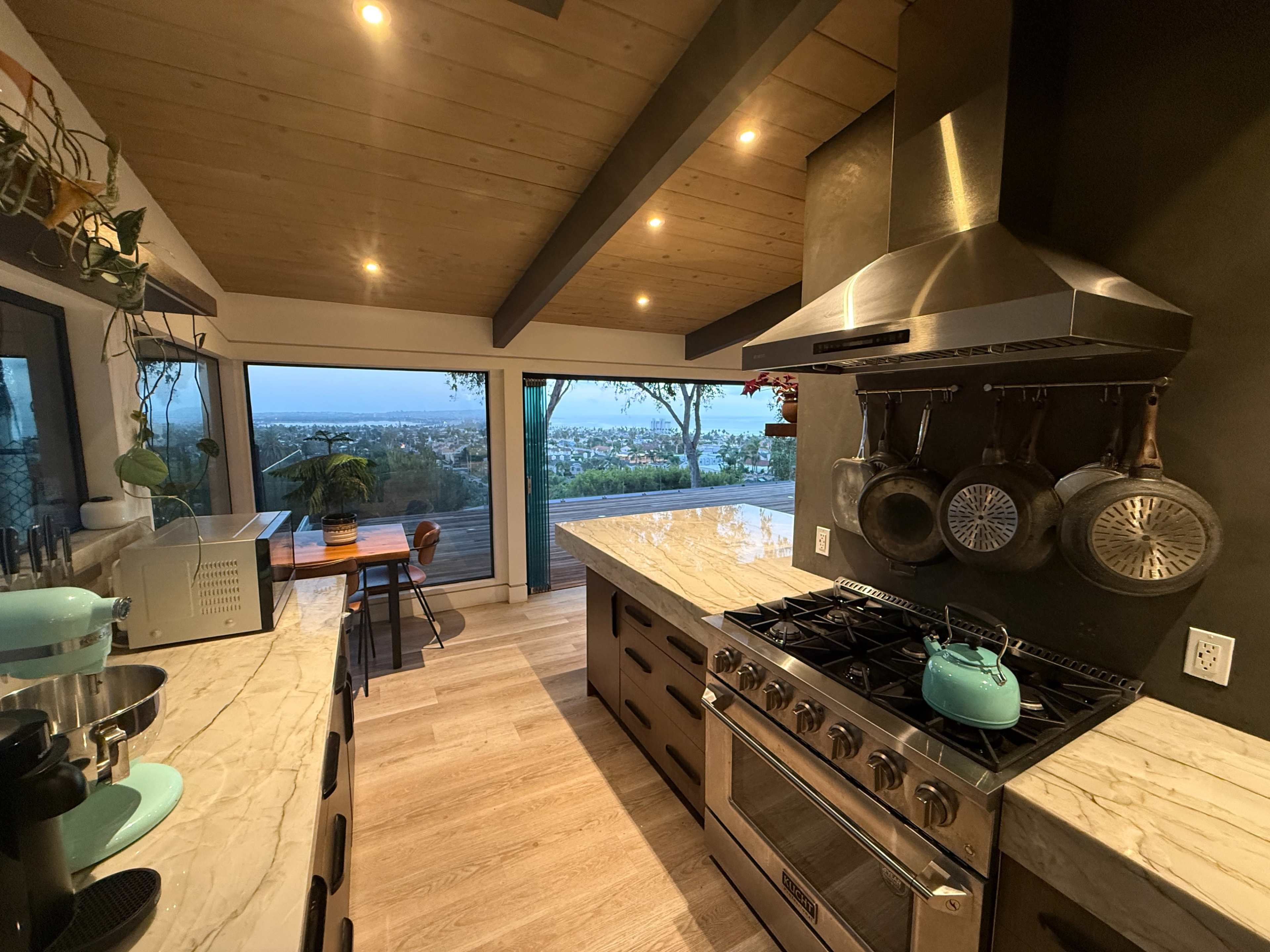 A modern kitchen features a marble countertop, stainless steel appliances, and a view of the outdoors through large windows.