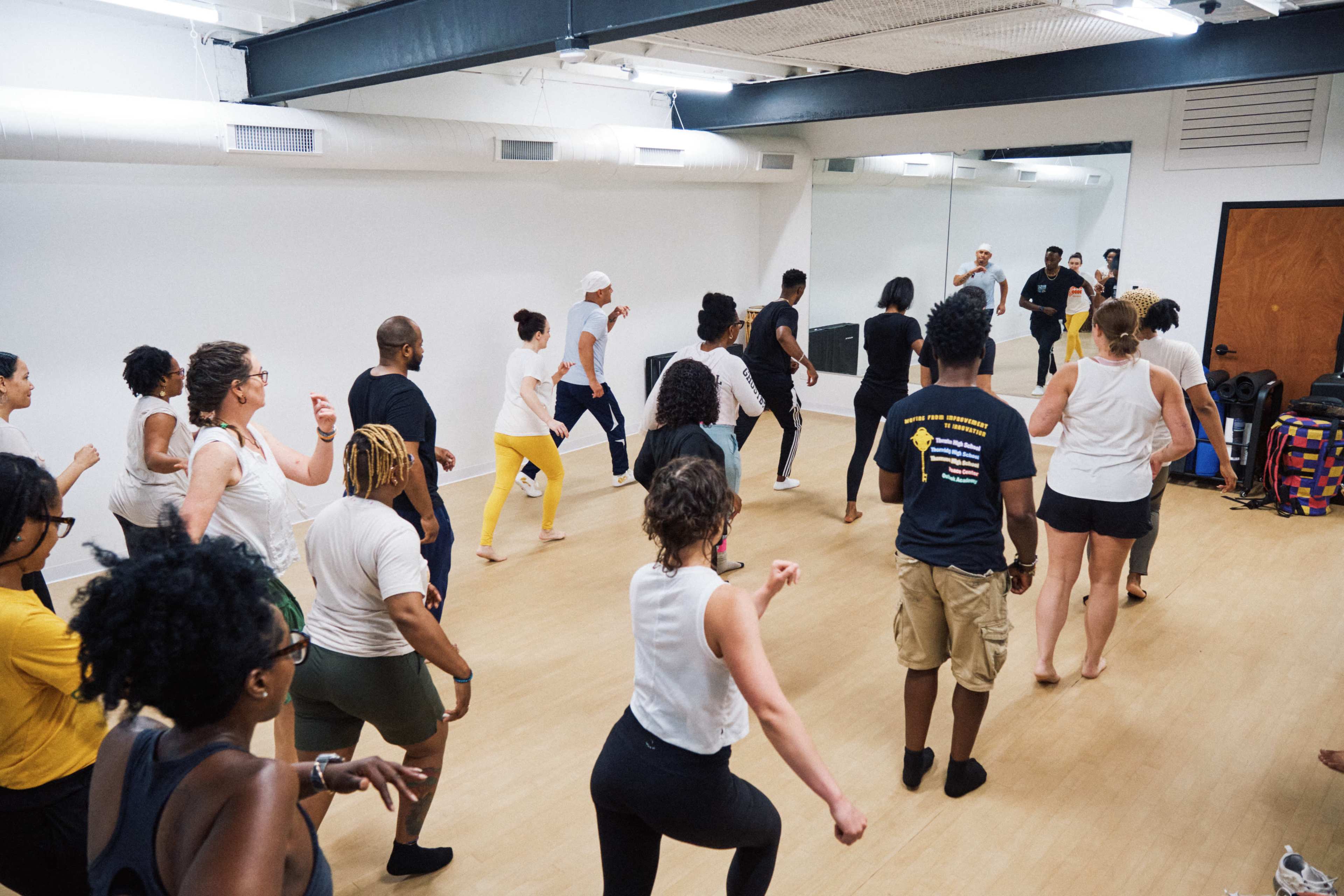 A group of individuals participates in a dance class in a spacious, mirrored studio.