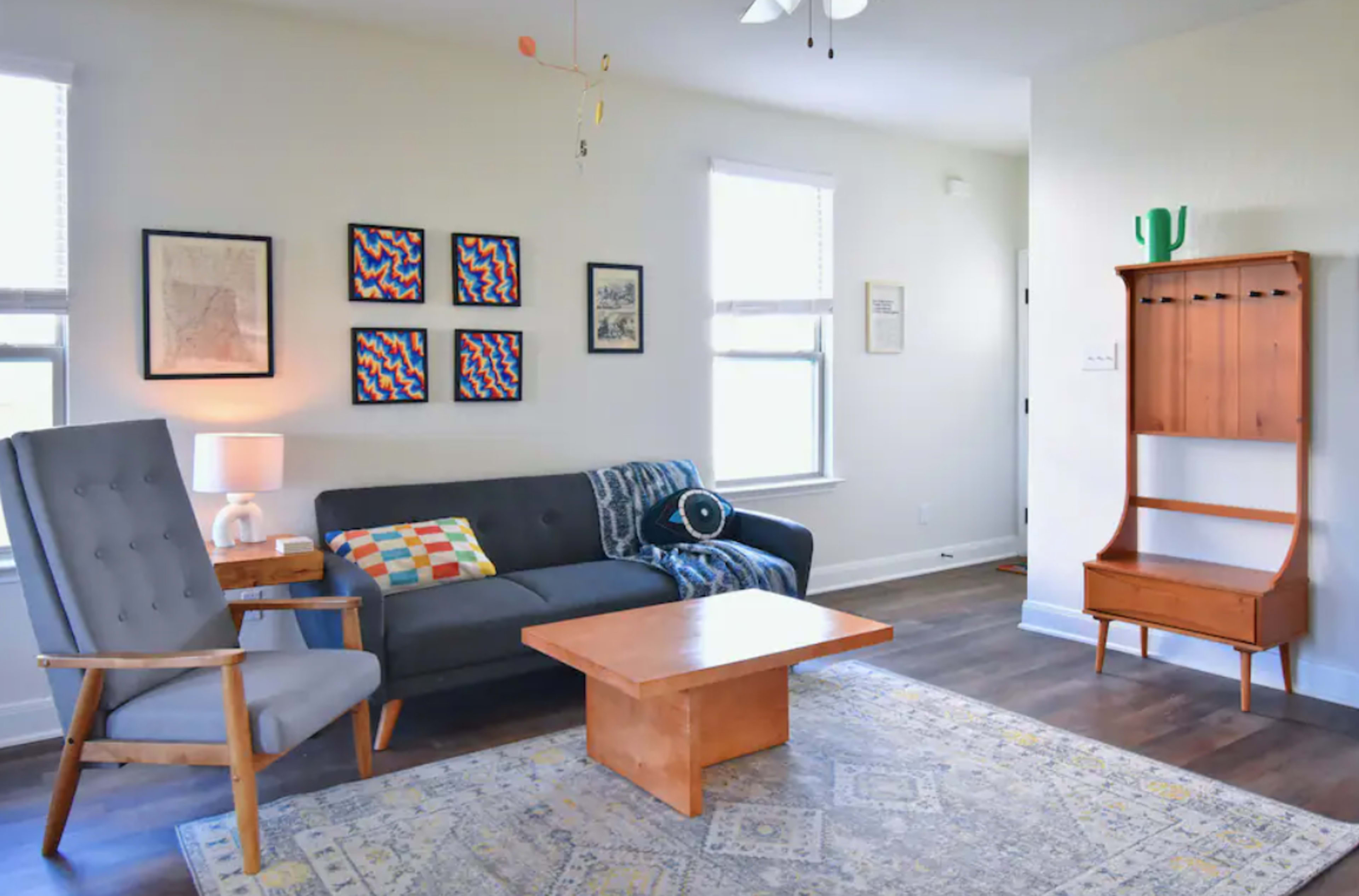 A modern living room featuring a gray sofa, two armchairs, a coffee table, patterned wall art, and a side table with a lamp.