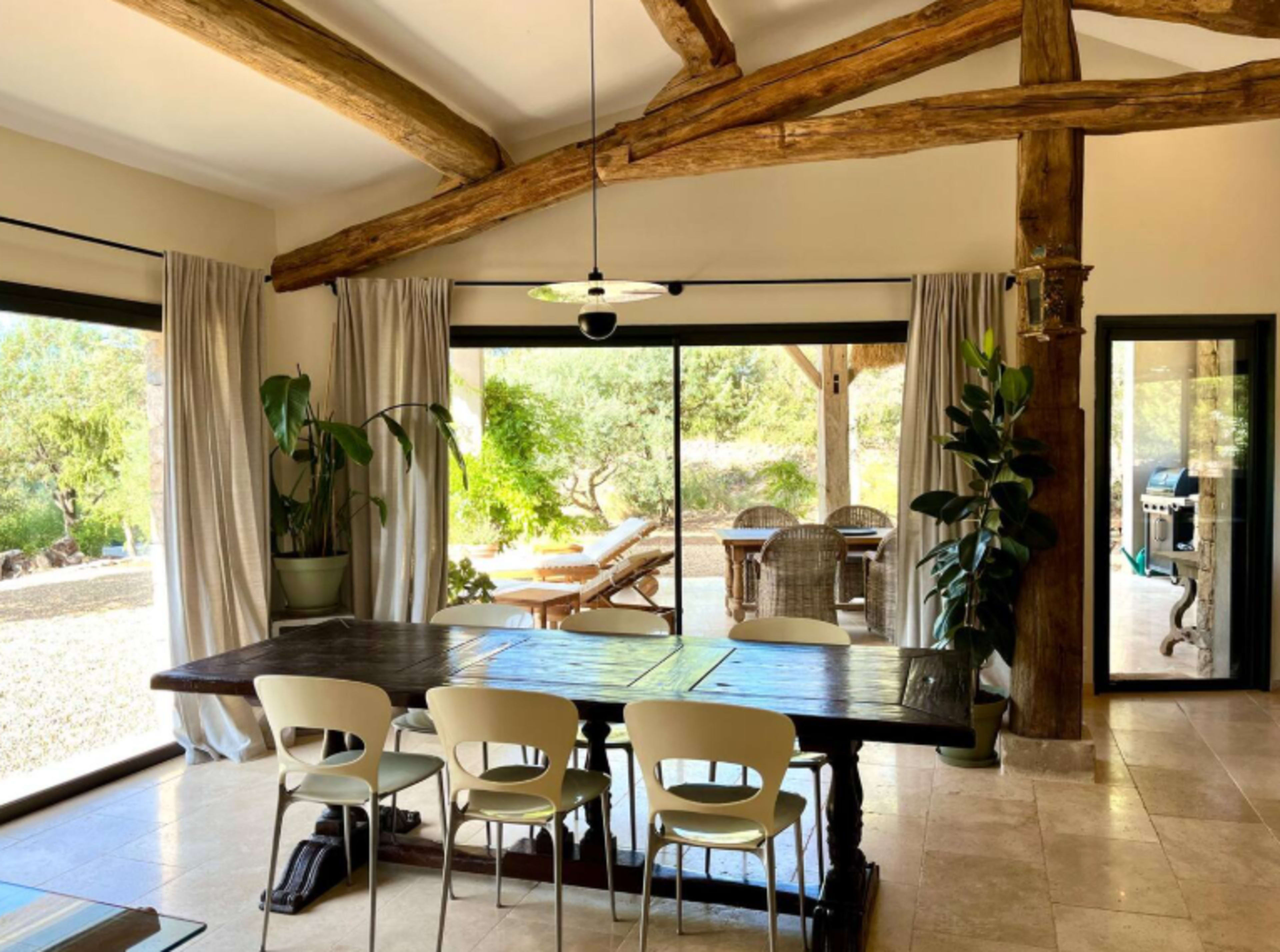 A spacious dining area features a large wooden table surrounded by white chairs, with large glass doors opening to a scenic outdoor patio.