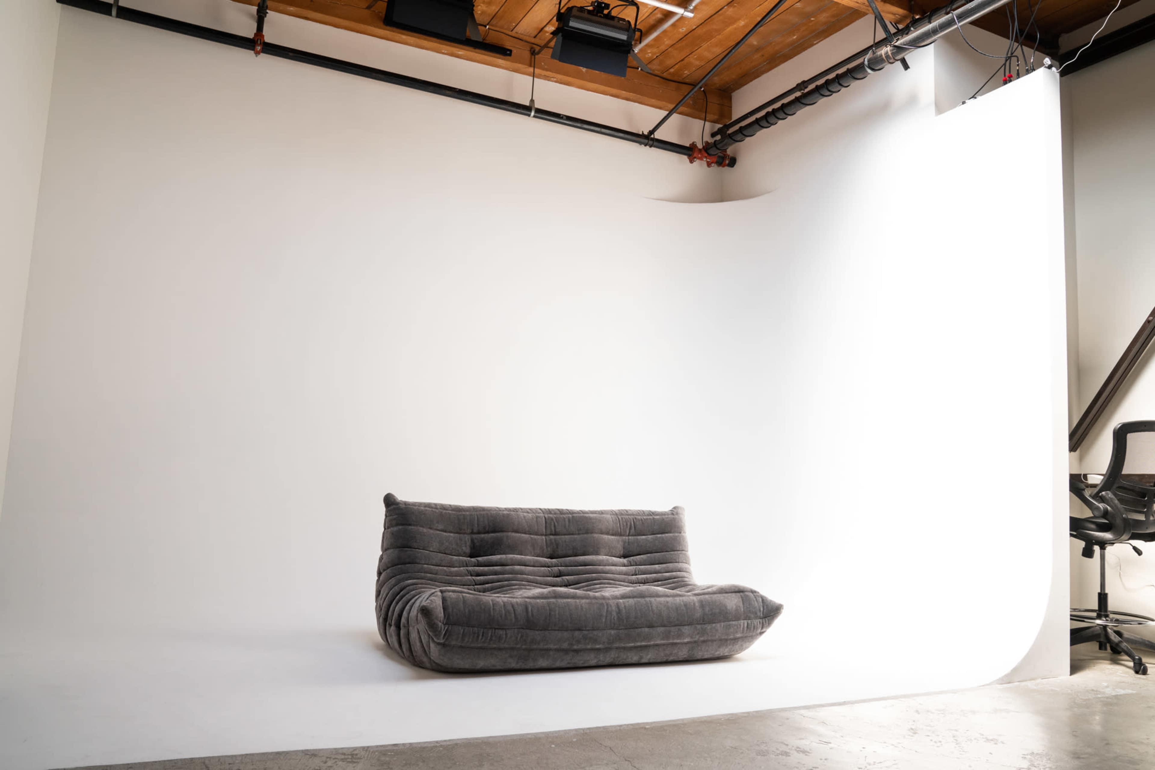 A gray sofa positioned in front of a white backdrop in a studio space.