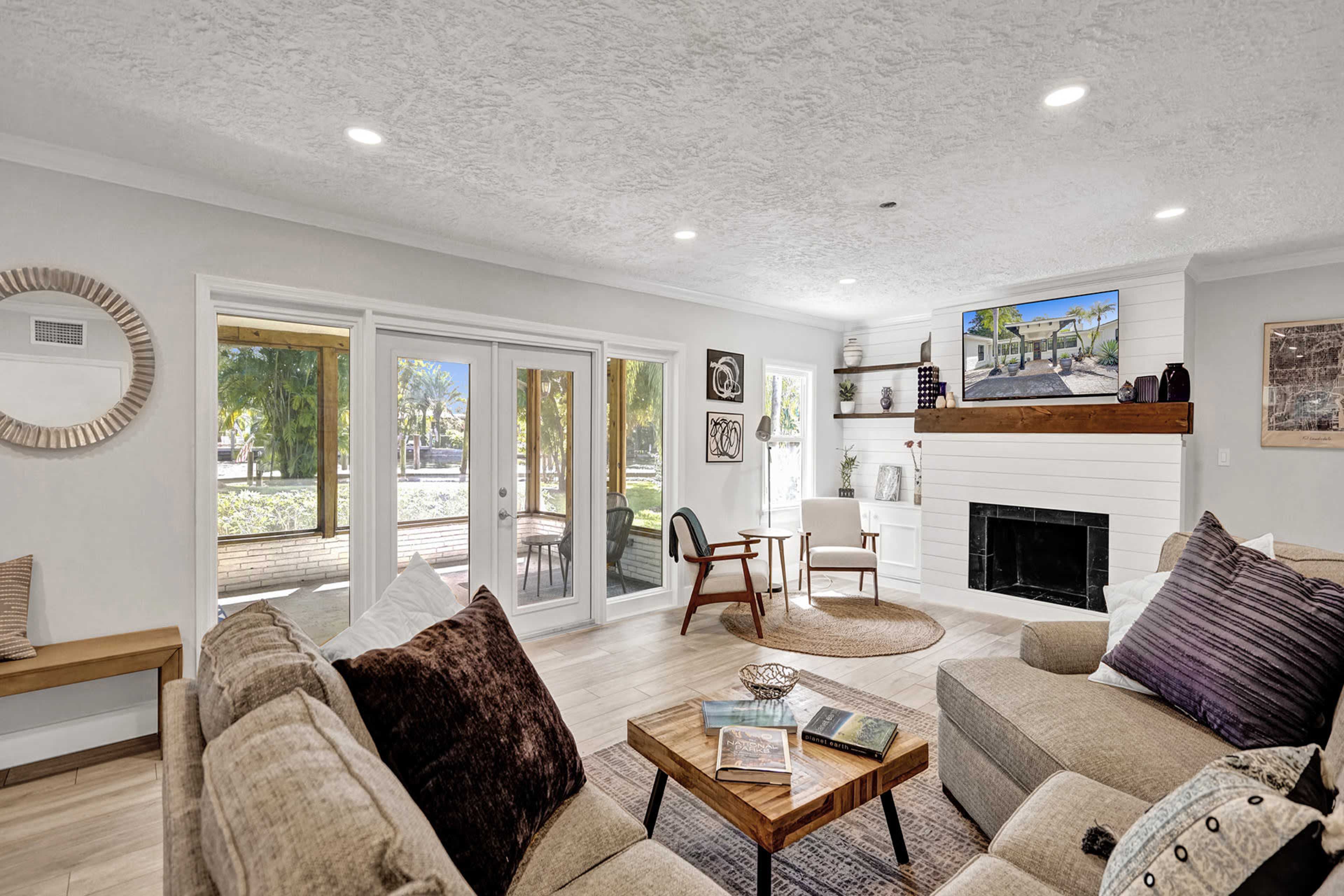 A spacious living room features a comfortable sectional sofa, a wooden coffee table, and a fireplace, with large windows providing views of an outdoor area.