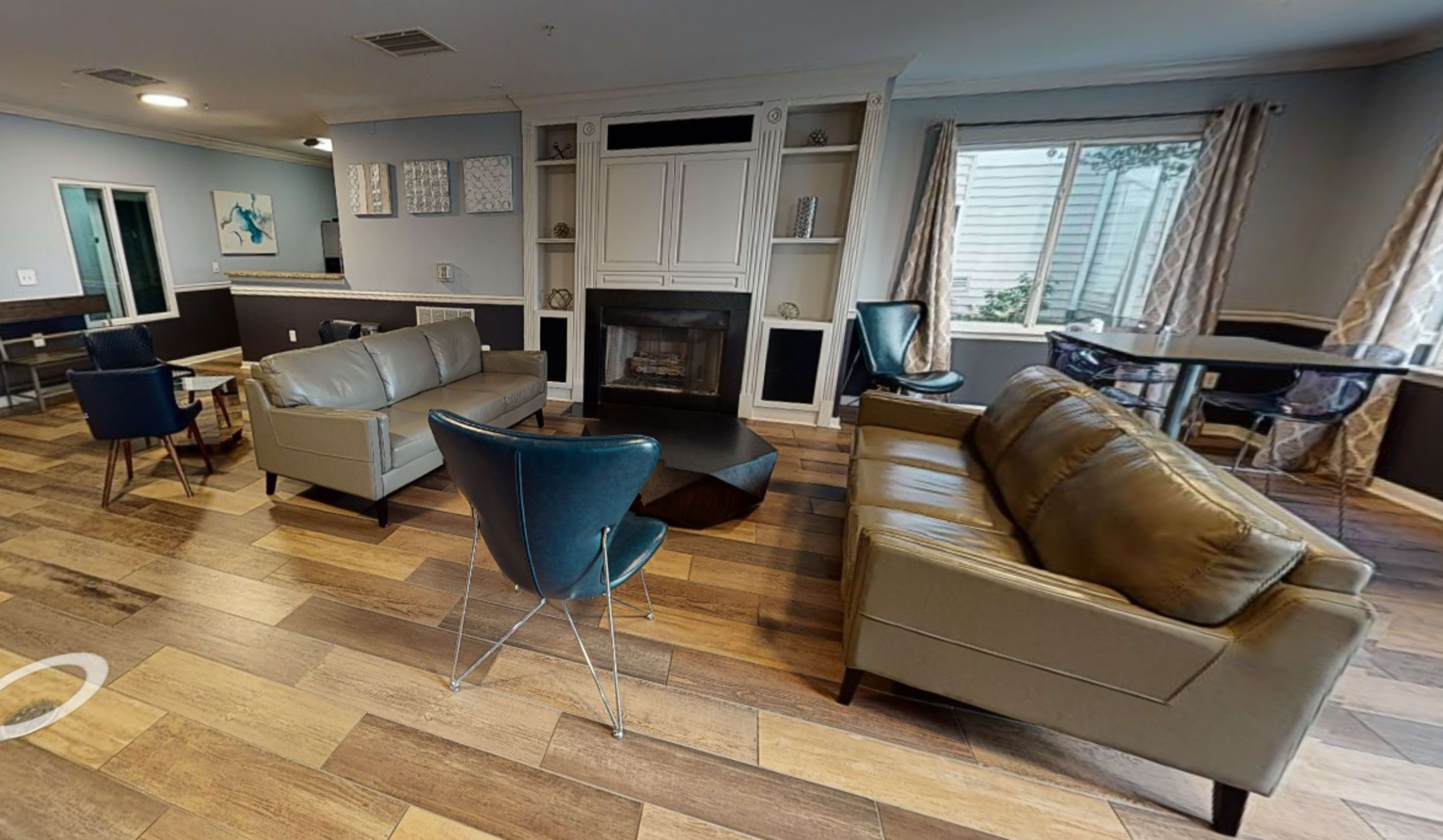 The living room features a fireplace, two leather sofas, several chairs, and a dining area with a table, all arranged around a central coffee table.