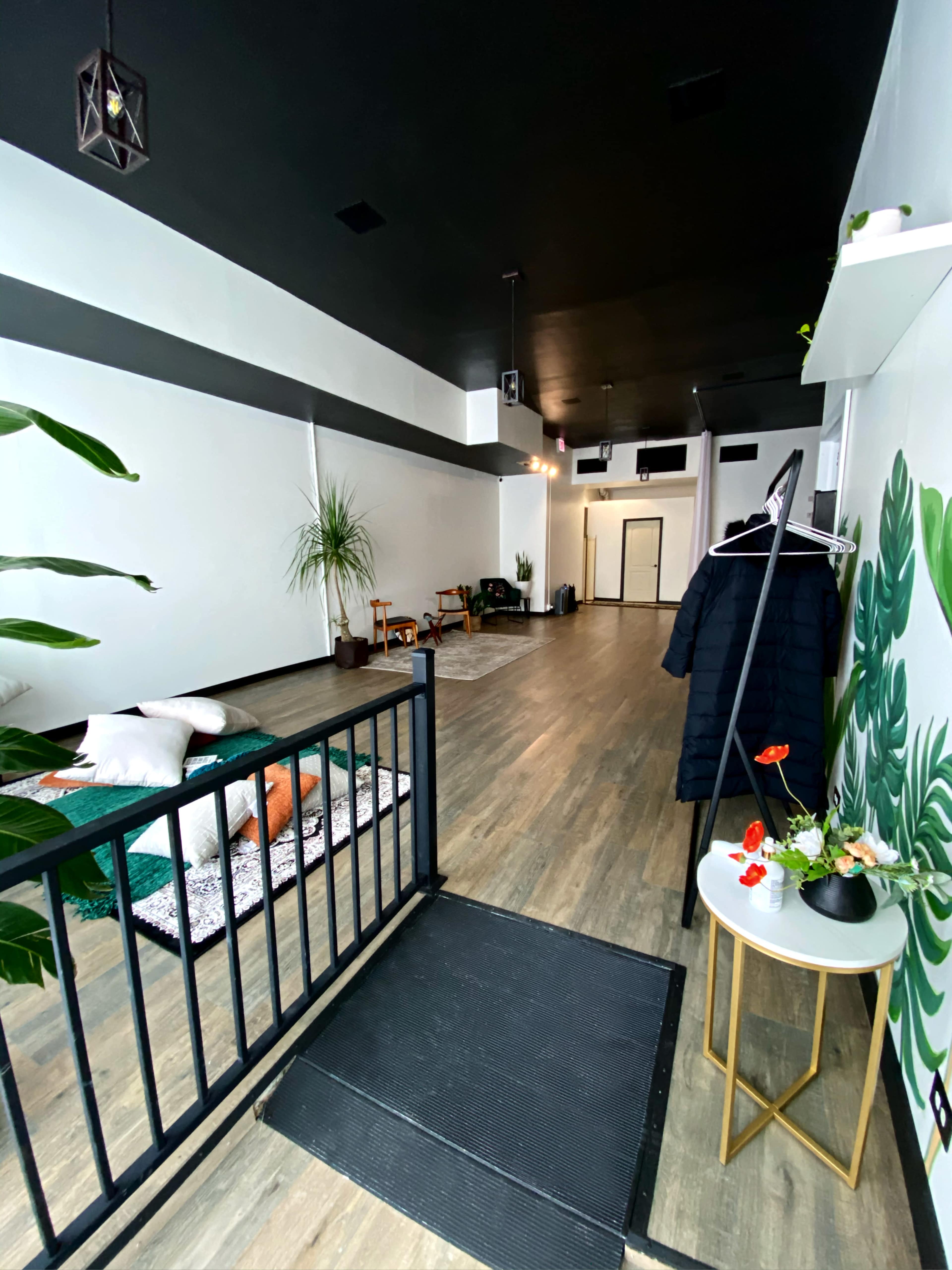 A spacious interior with a black ceiling, wooden flooring, and minimal furniture, including a seating area and decorative plants.