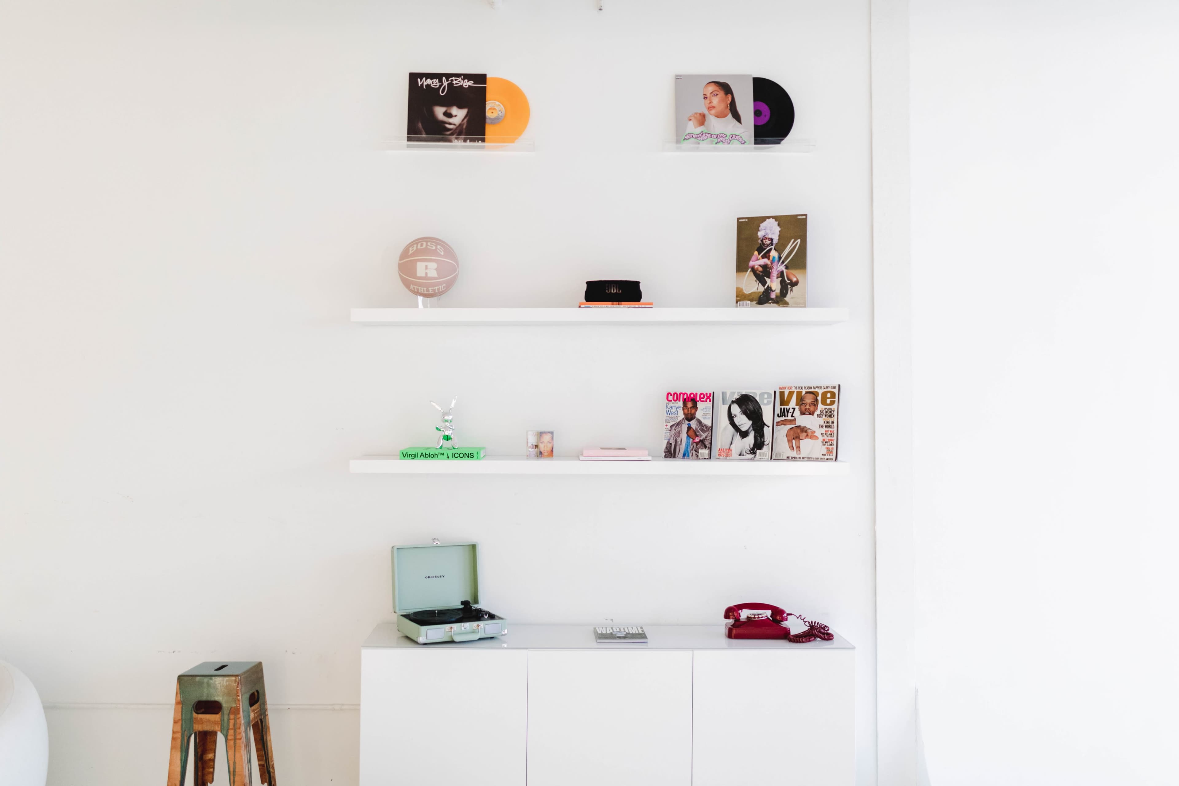 A minimalist wall display features vinyl records, magazines, and a vintage record player on a console table.