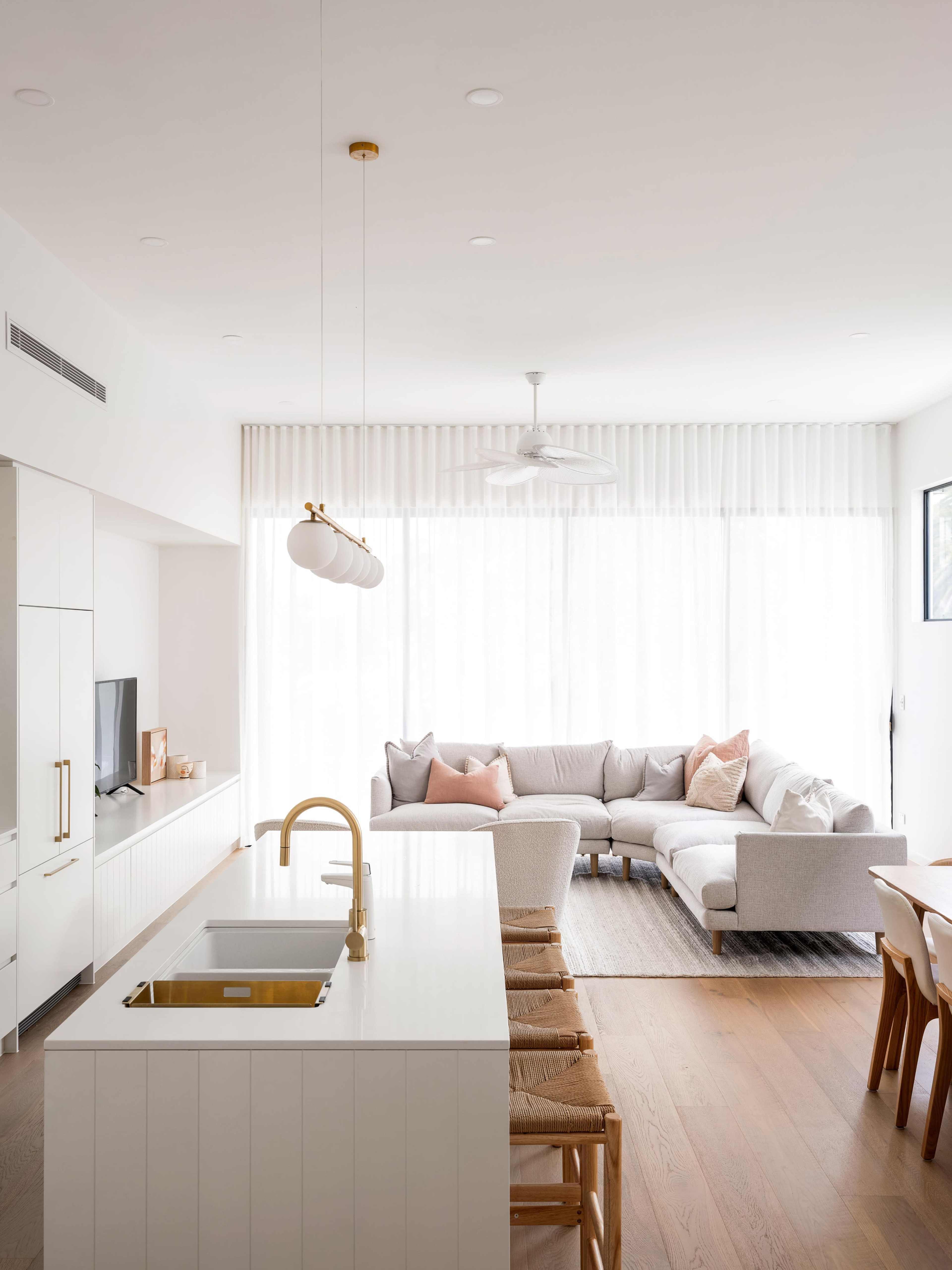 A modern, open living space features a light-filled area with a sectional sofa, dining table, and a kitchen island with bar stools.