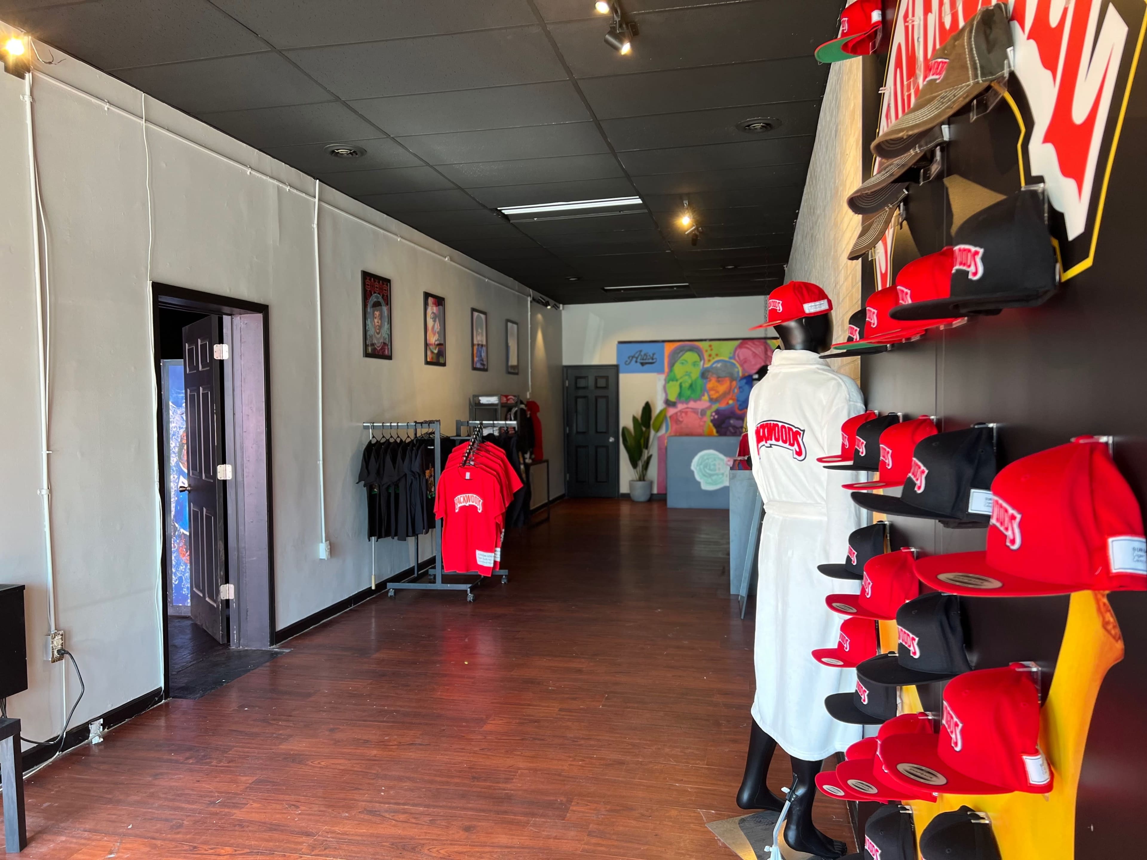 The interior of a retail store features a row of red hats displayed on a wall and shirts hanging on racks along the left side.