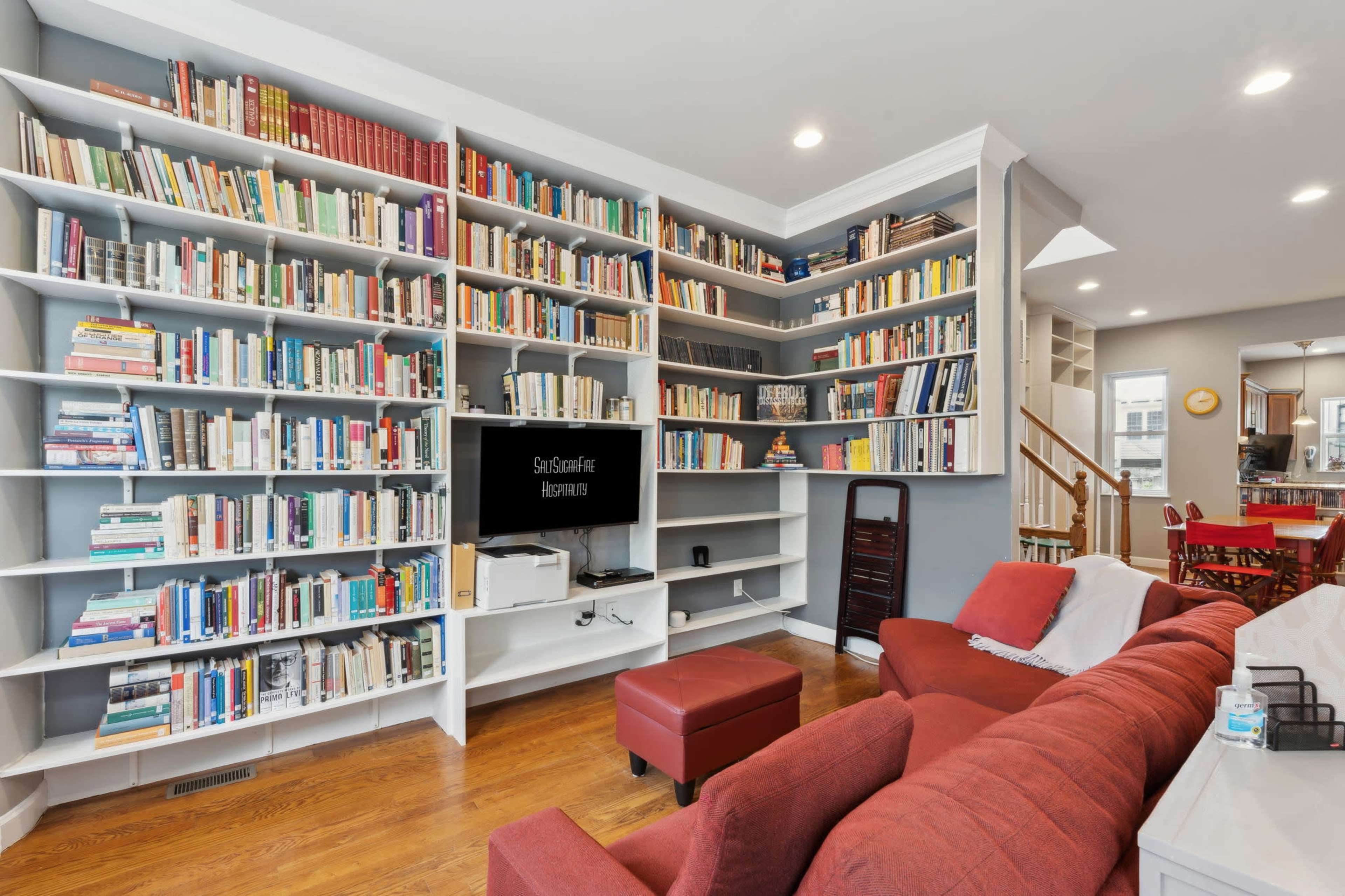 A cozy living room features a large wall of bookshelves filled with books, a television, and a red couch with an ottoman.