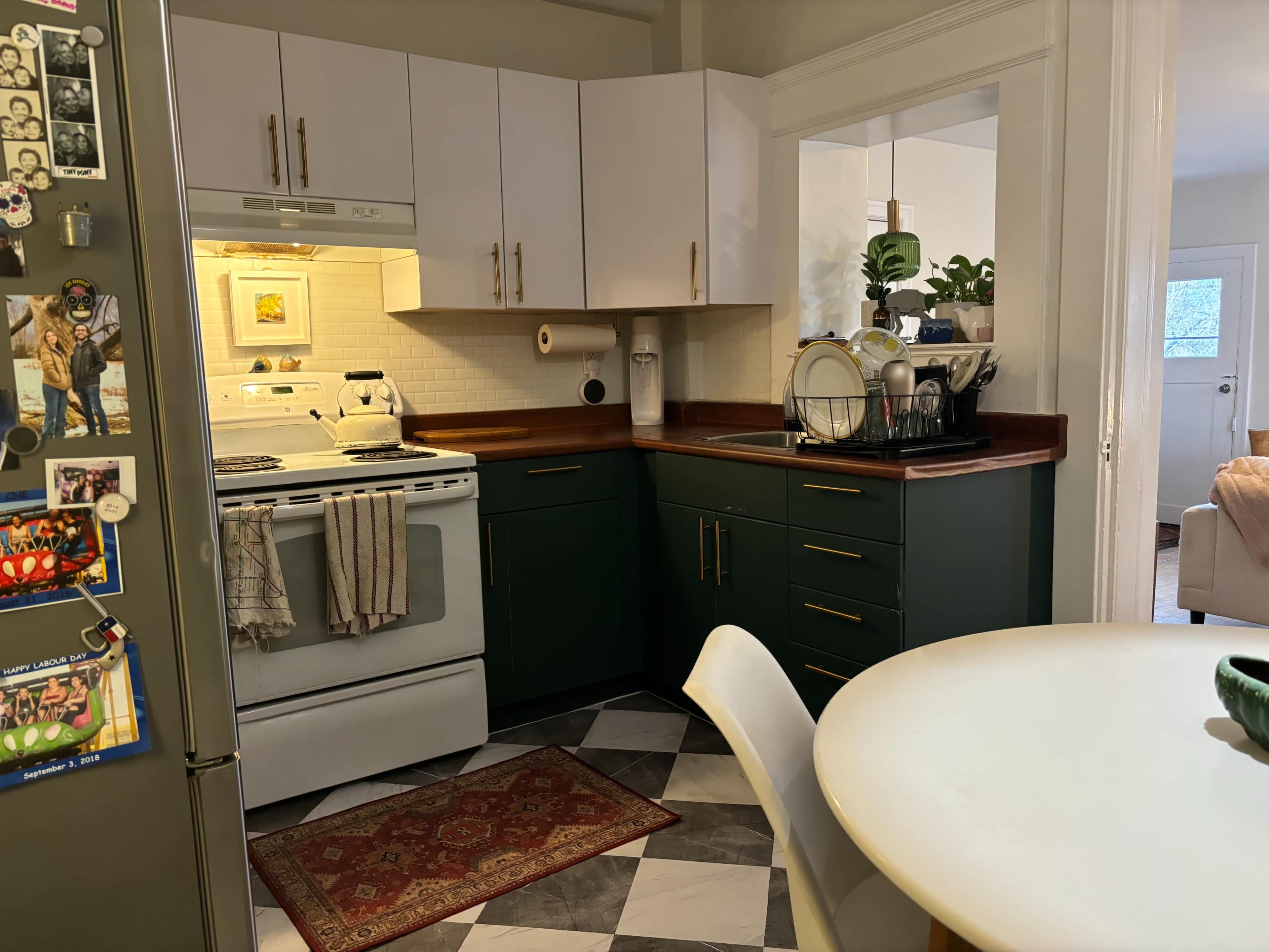 A kitchen with white and green cabinets, a stove, and a dining table on a patterned floor.