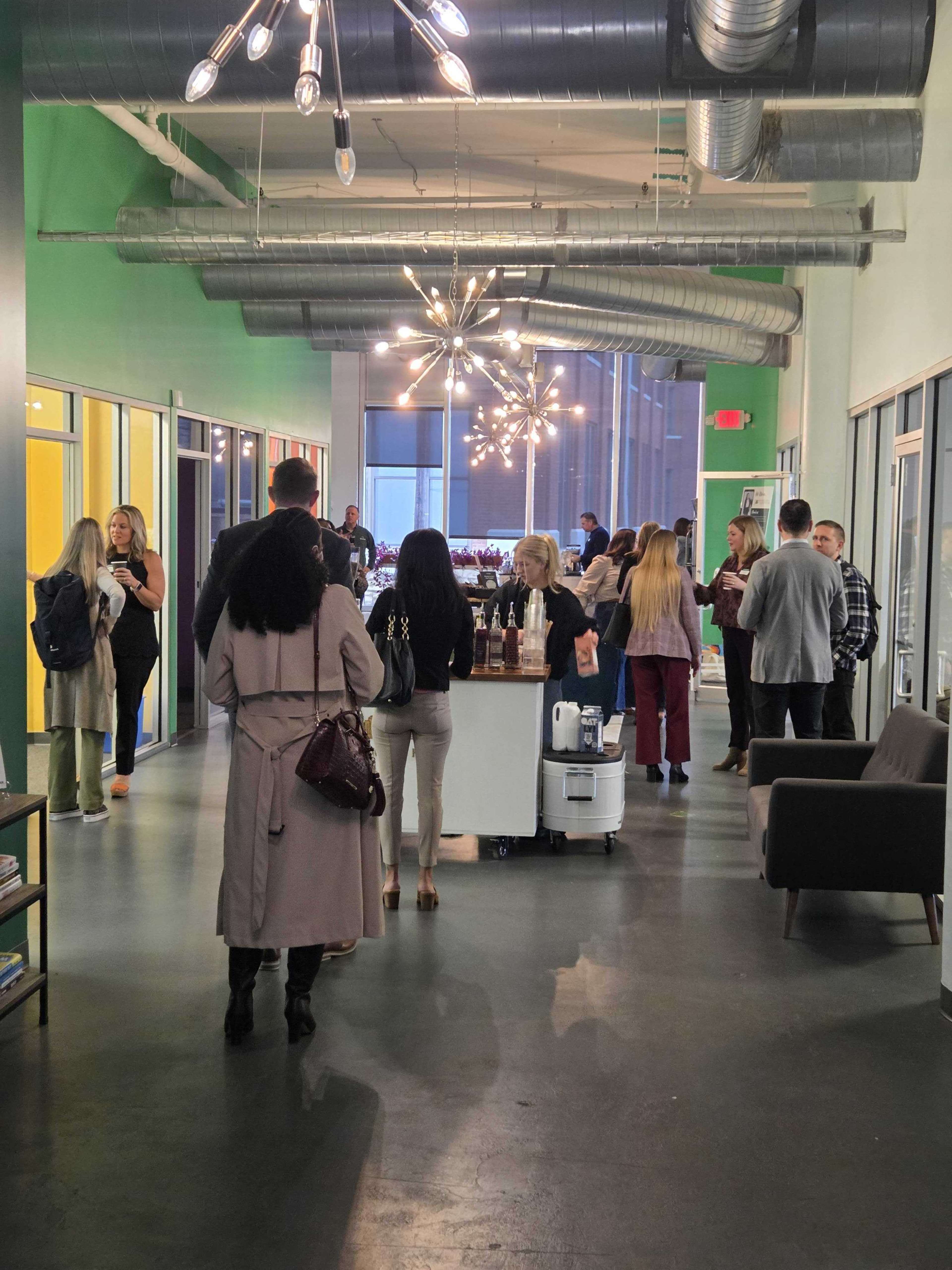 A group of people is gathered in a well-lit hallway with modern decor, engaging in conversation near a display table.