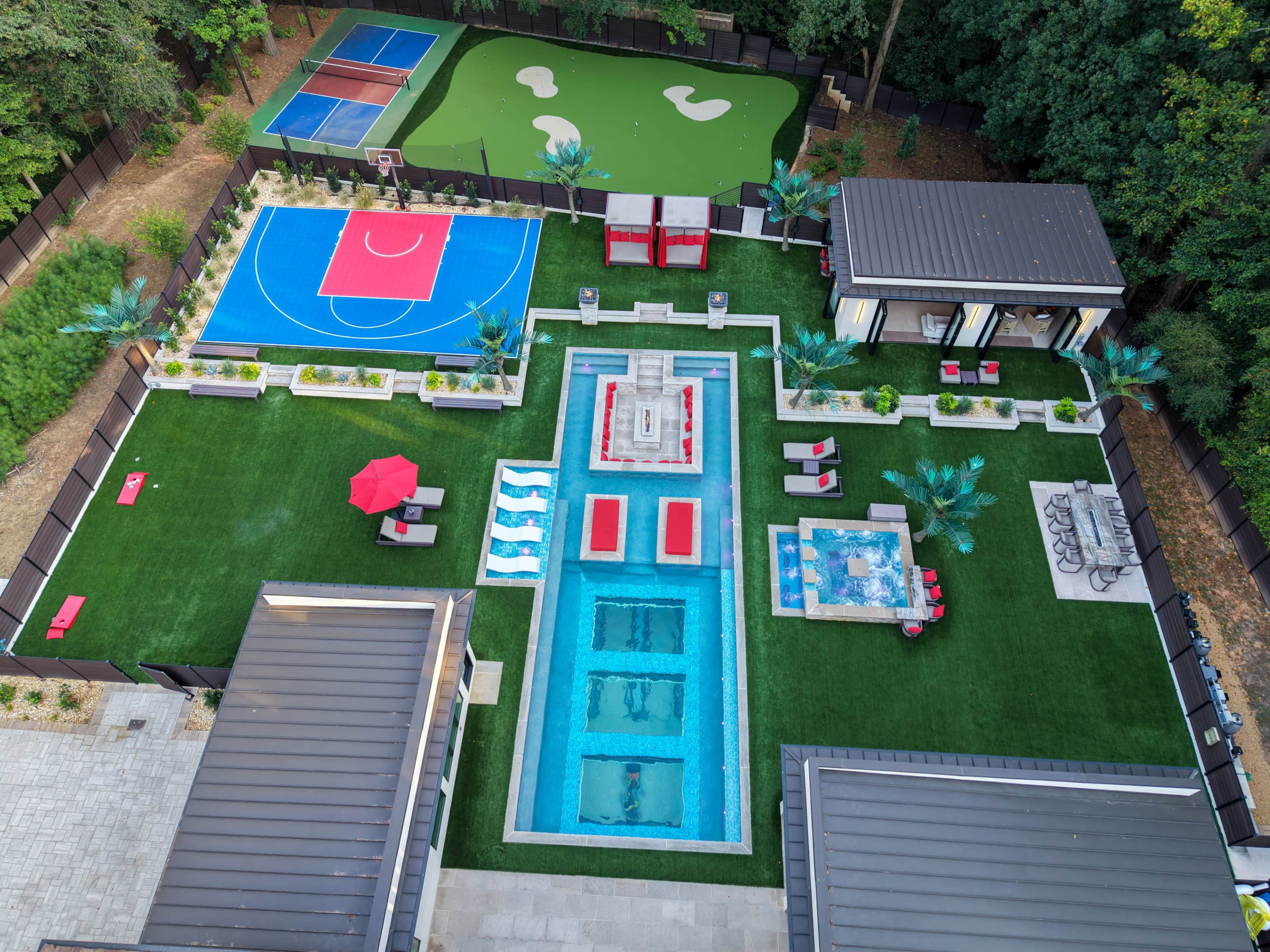 The image shows a spacious outdoor area featuring a swimming pool, a basketball court, a putting green, and various seating arrangements surrounded by landscaping.