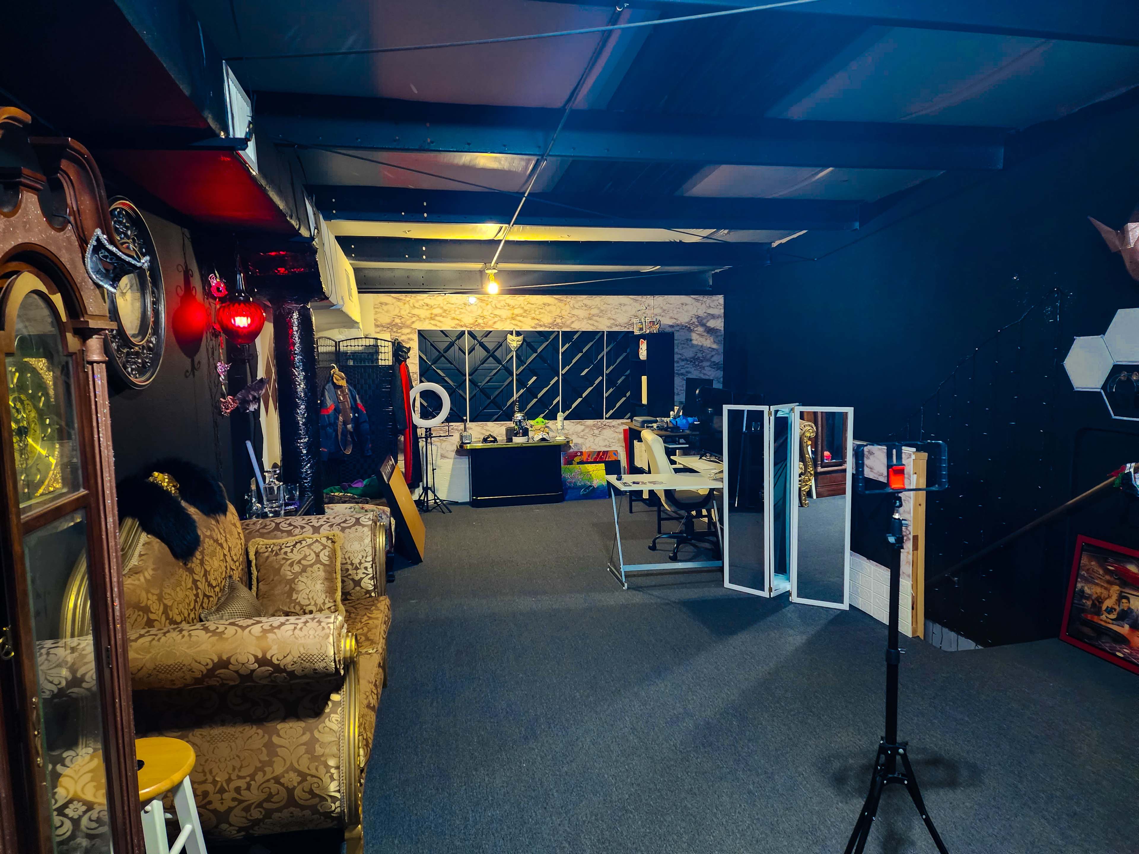 A spacious interior room with a sofa, a desk area, and partitions dividing different sections, all set against dark walls and a carpeted floor.