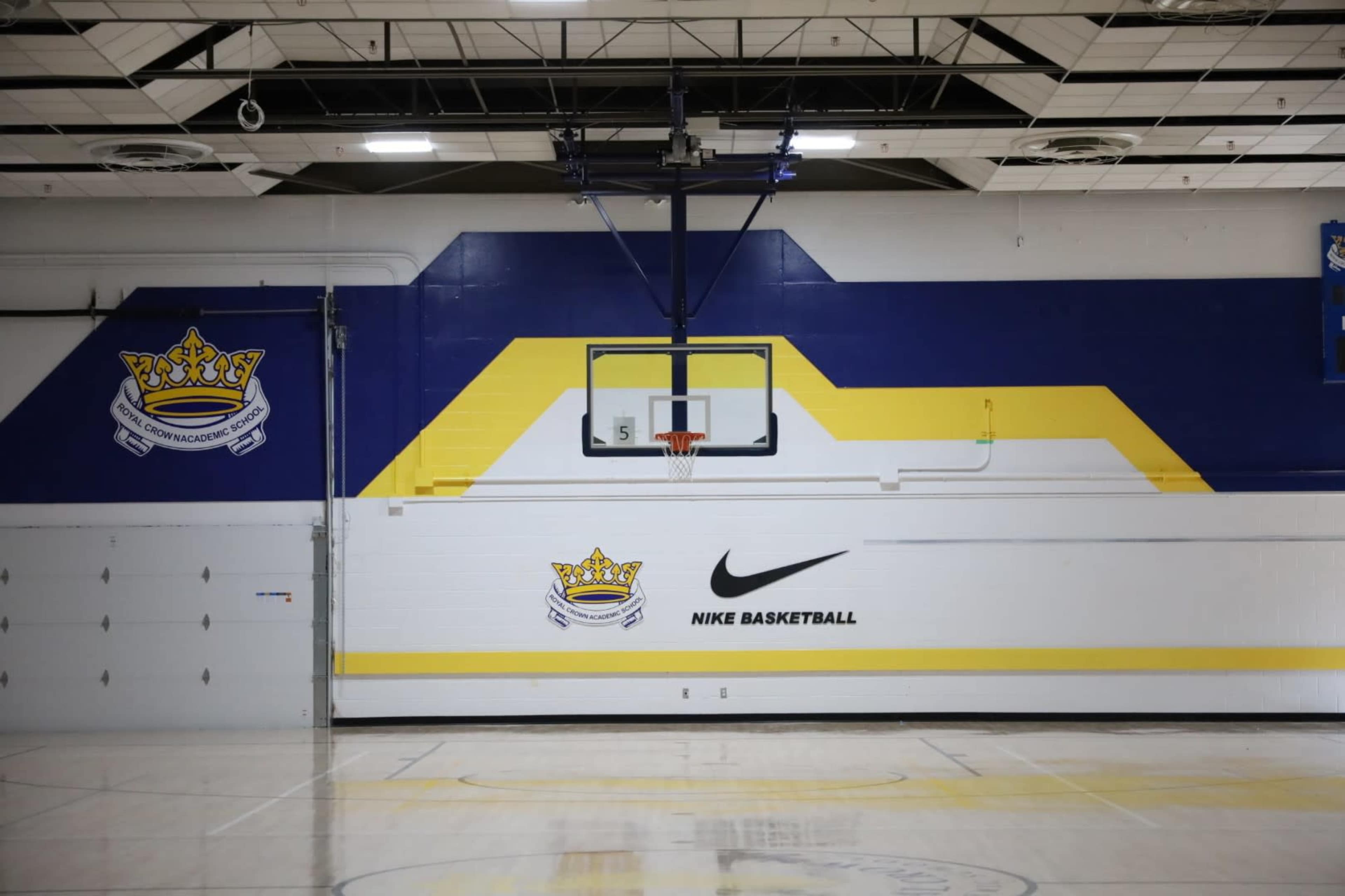 The image shows a basketball court with a hoop against a colorful wall that features a crown logo and the Nike Basketball branding.