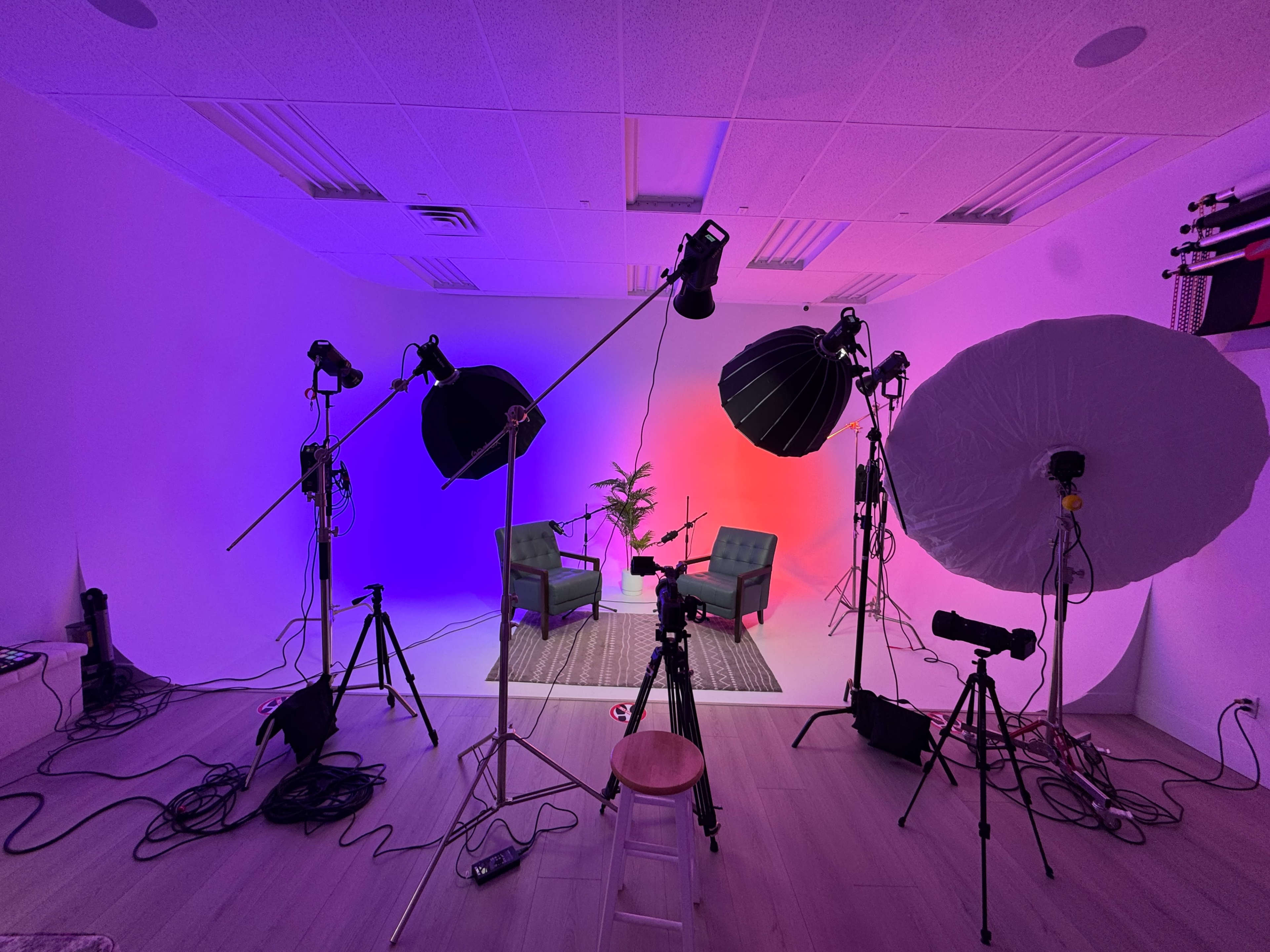 A photography studio is set up with lights, backdrops, and two chairs in front of a gradient-colored wall.