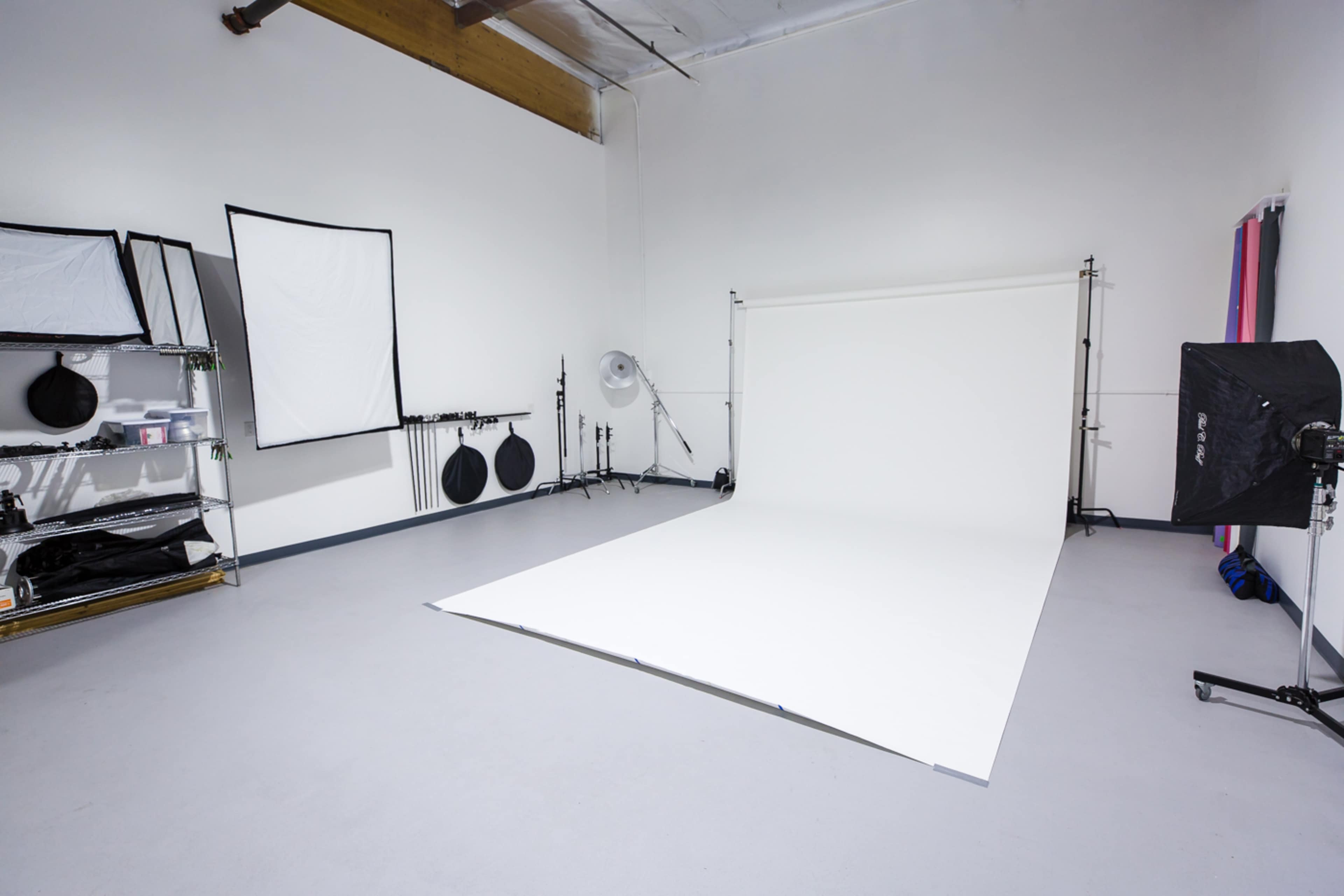 A photography studio equipped with a white backdrop, lighting equipment, and various photography accessories organized on shelving.