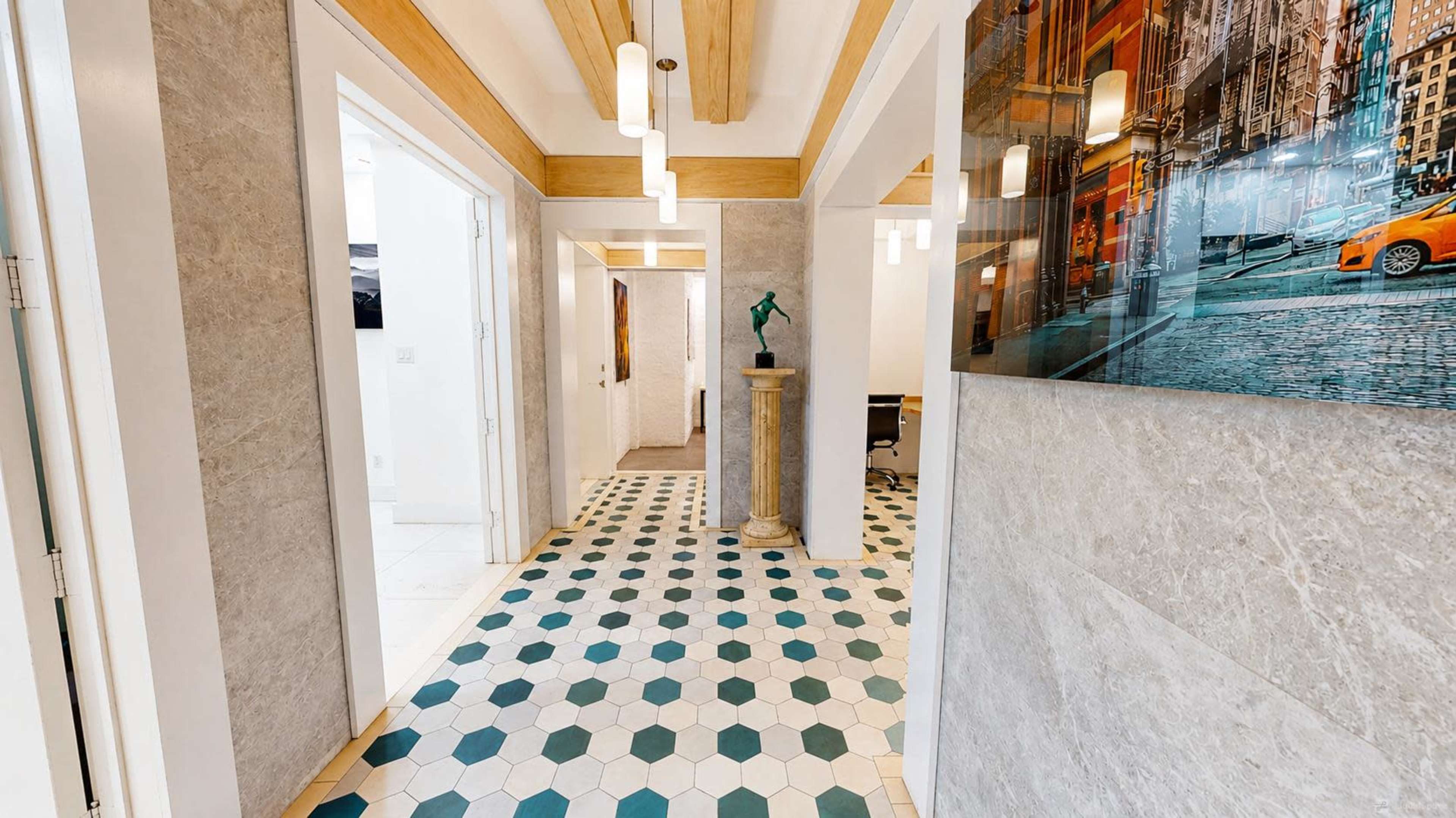 The image shows a hallway with patterned tile flooring, featuring hexagonal shapes in green and white, and framed artwork on the walls.