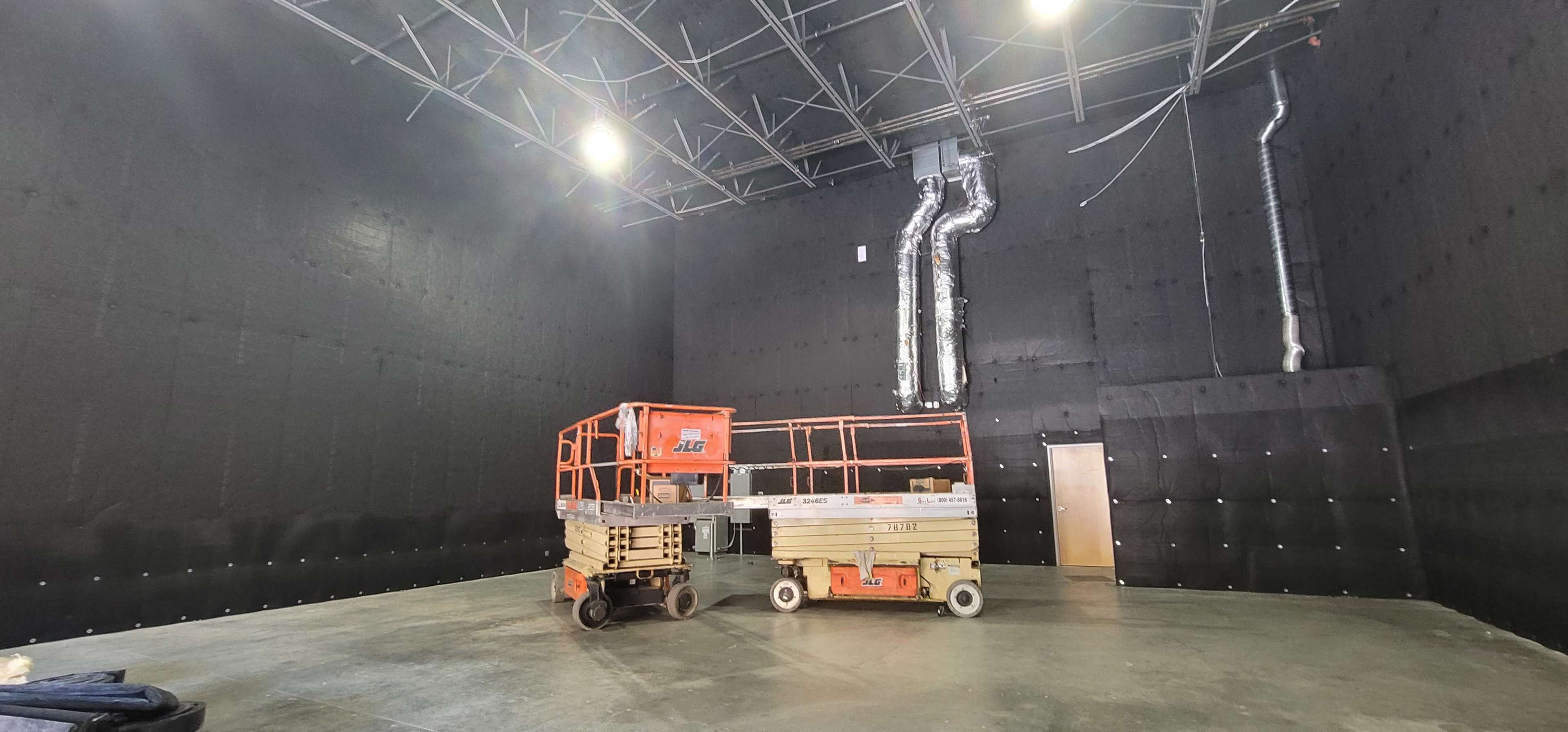 A large, empty room with black walls and two scissor lift platforms positioned on the concrete floor.