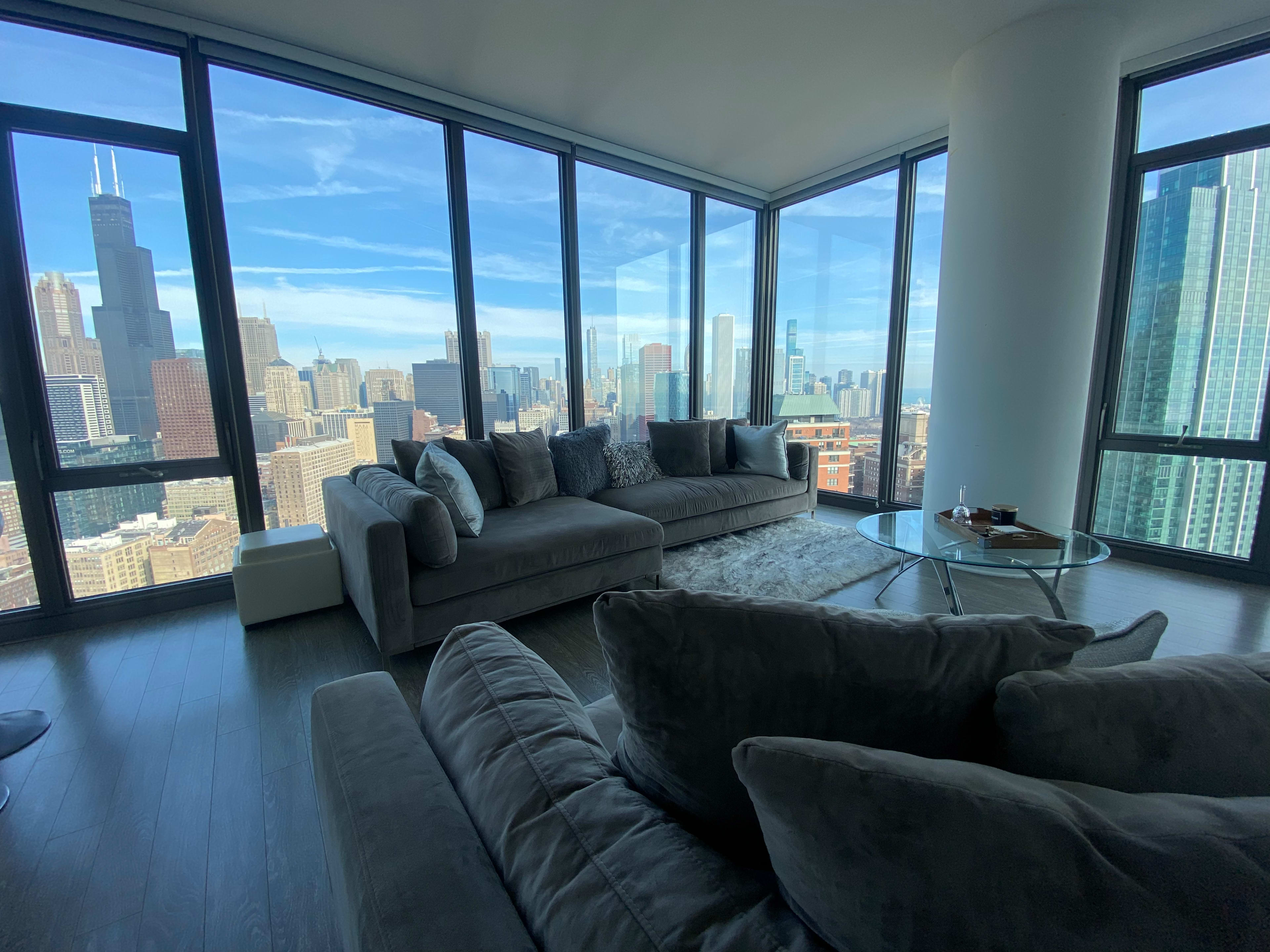 A modern living room with large windows overlooking a city skyline, featuring a sectional sofa and a glass coffee table.