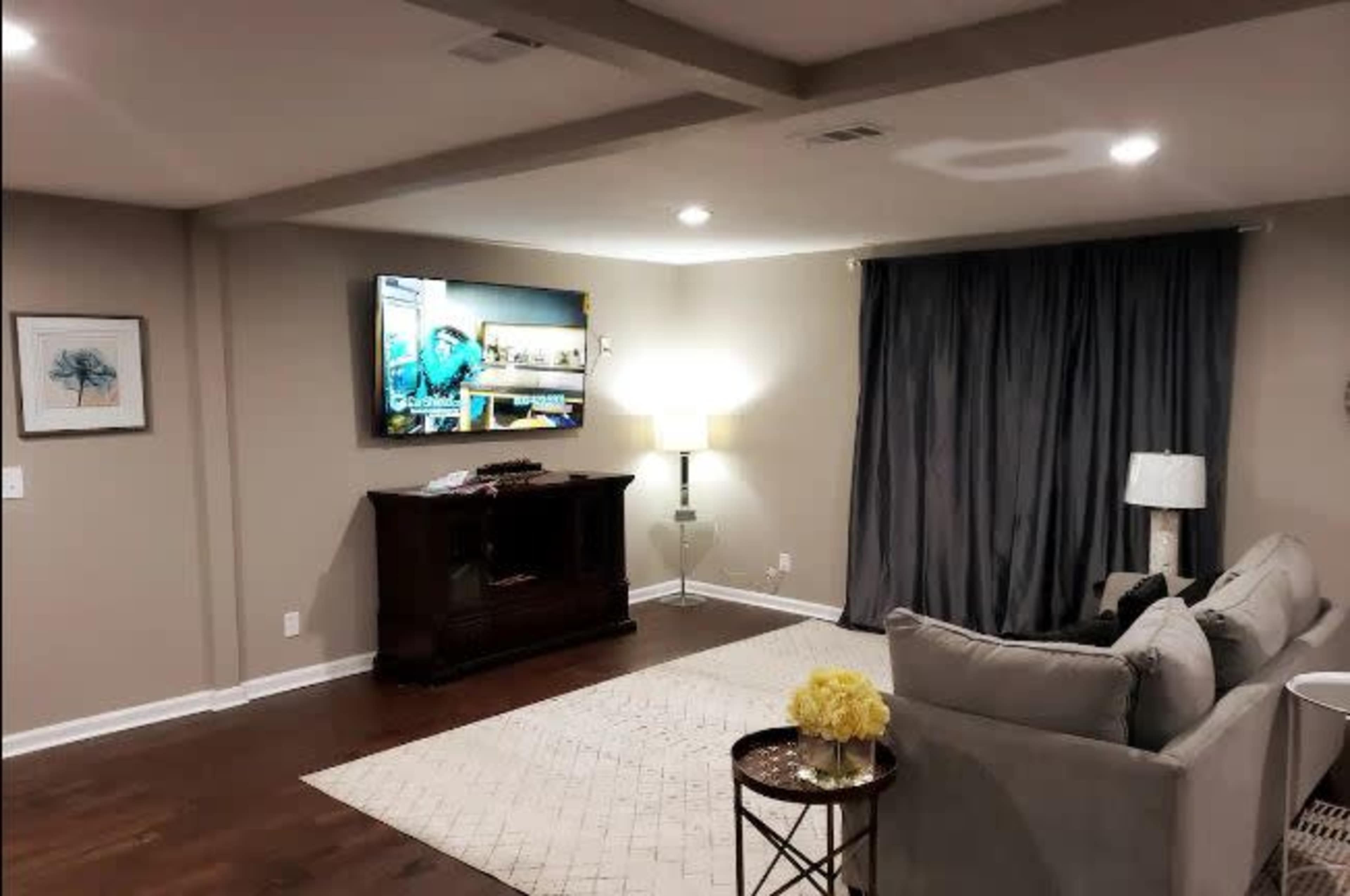 A modern living room featuring a gray sofa, a large television mounted on the wall, and a side table with a yellow floral arrangement.