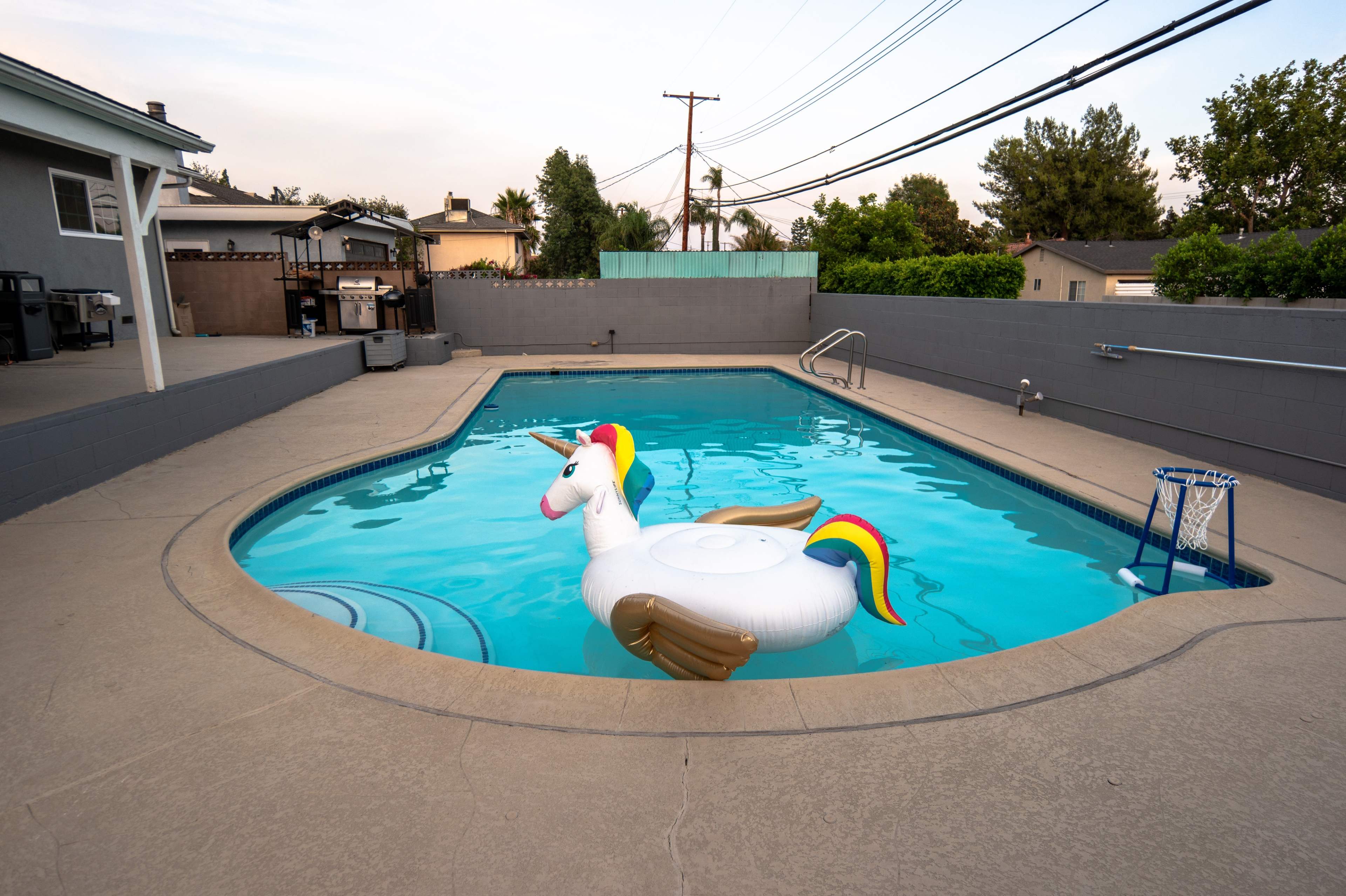 A large inflatable unicorn floats in a residential swimming pool surrounded by a concrete deck and gray walls.