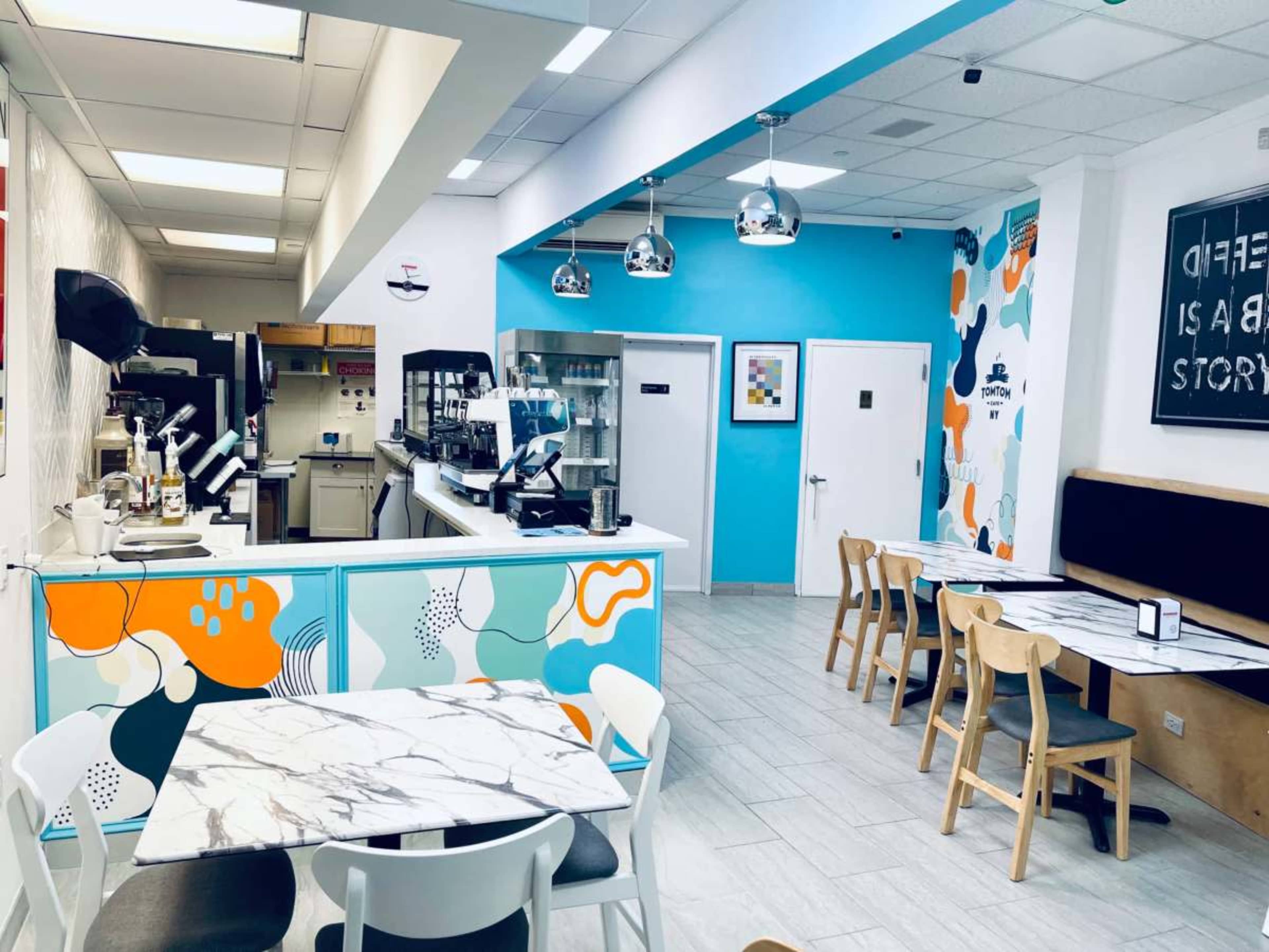 The image shows a brightly colored café interior with modern furniture, featuring a marble-topped table and a serving counter in the background.