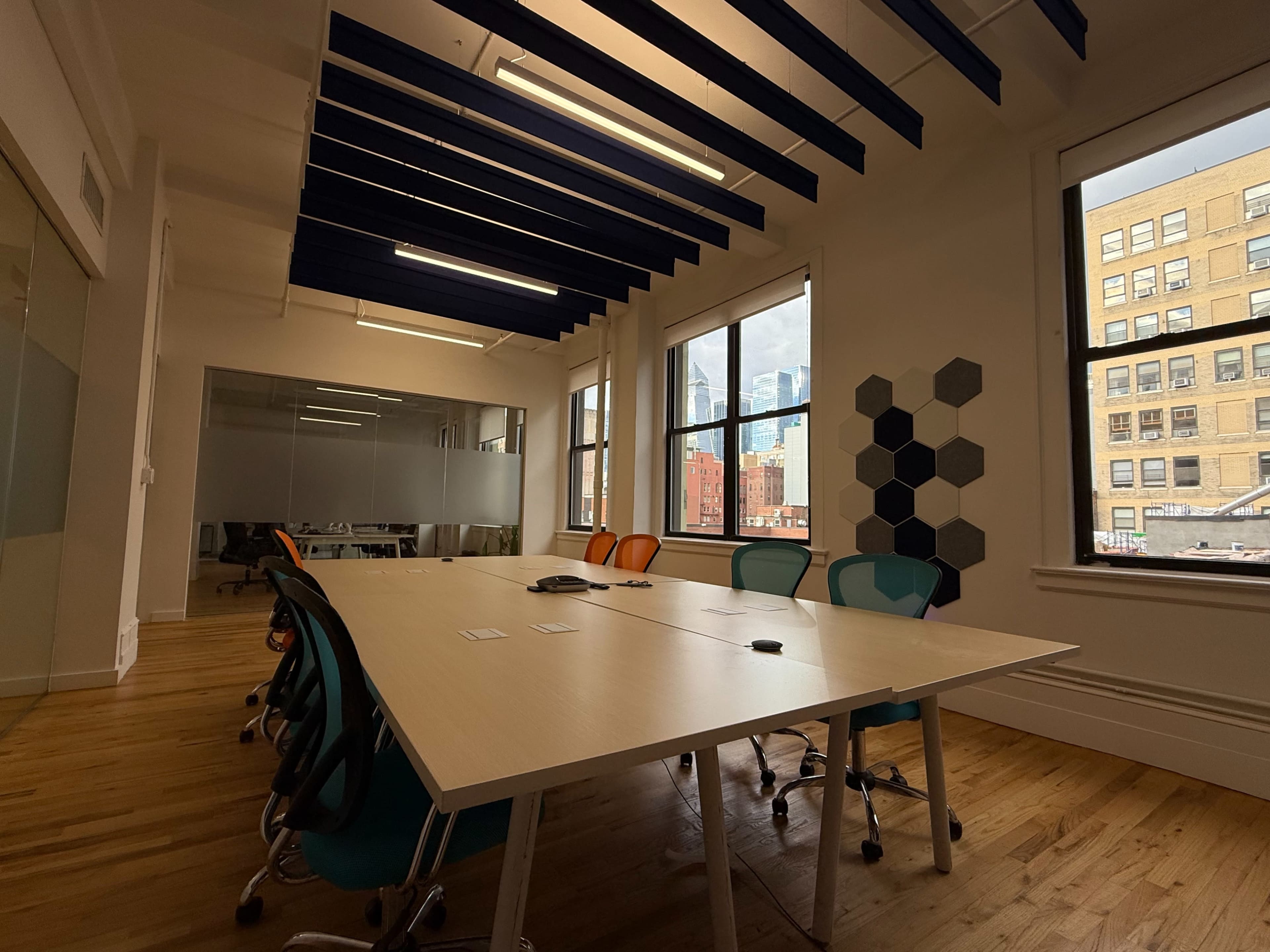 A modern conference room features a large table surrounded by colorful chairs, with large windows providing a view of the city skyline.