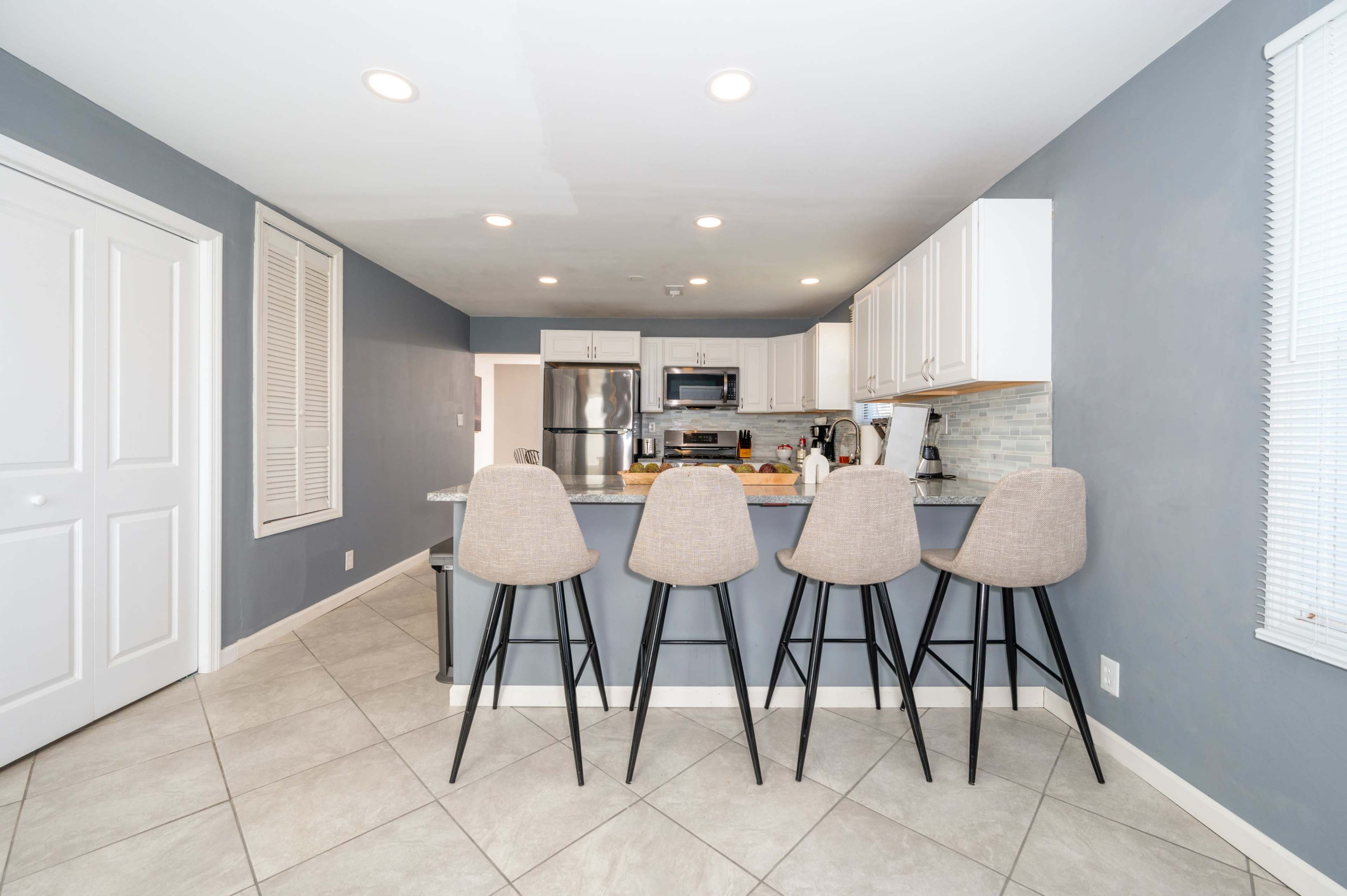 A modern kitchen features a gray color scheme with white cabinets and four high stools positioned at a breakfast bar.