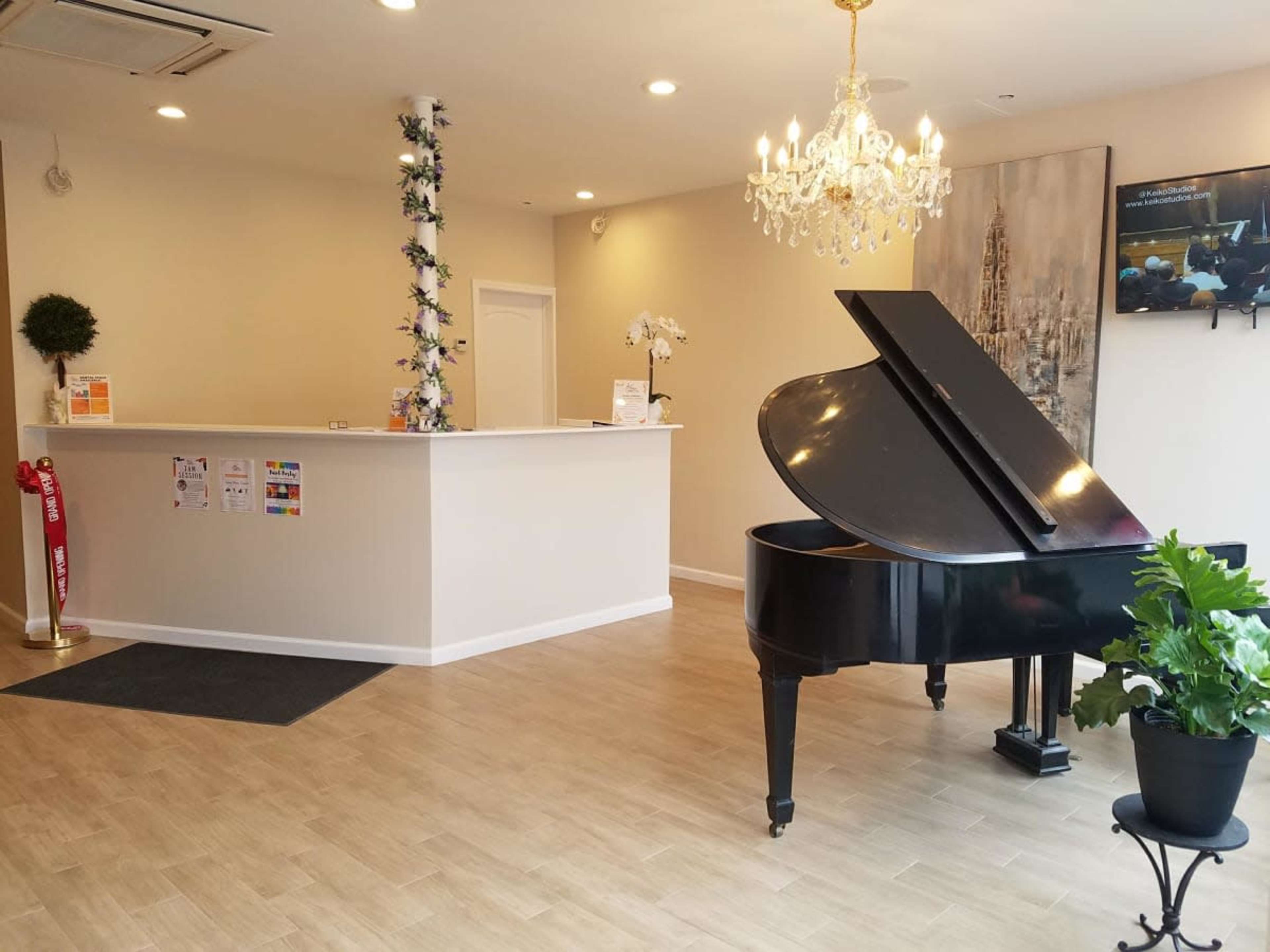 The image shows a modern reception area featuring a black grand piano, a chandelier, and a light-colored service counter.