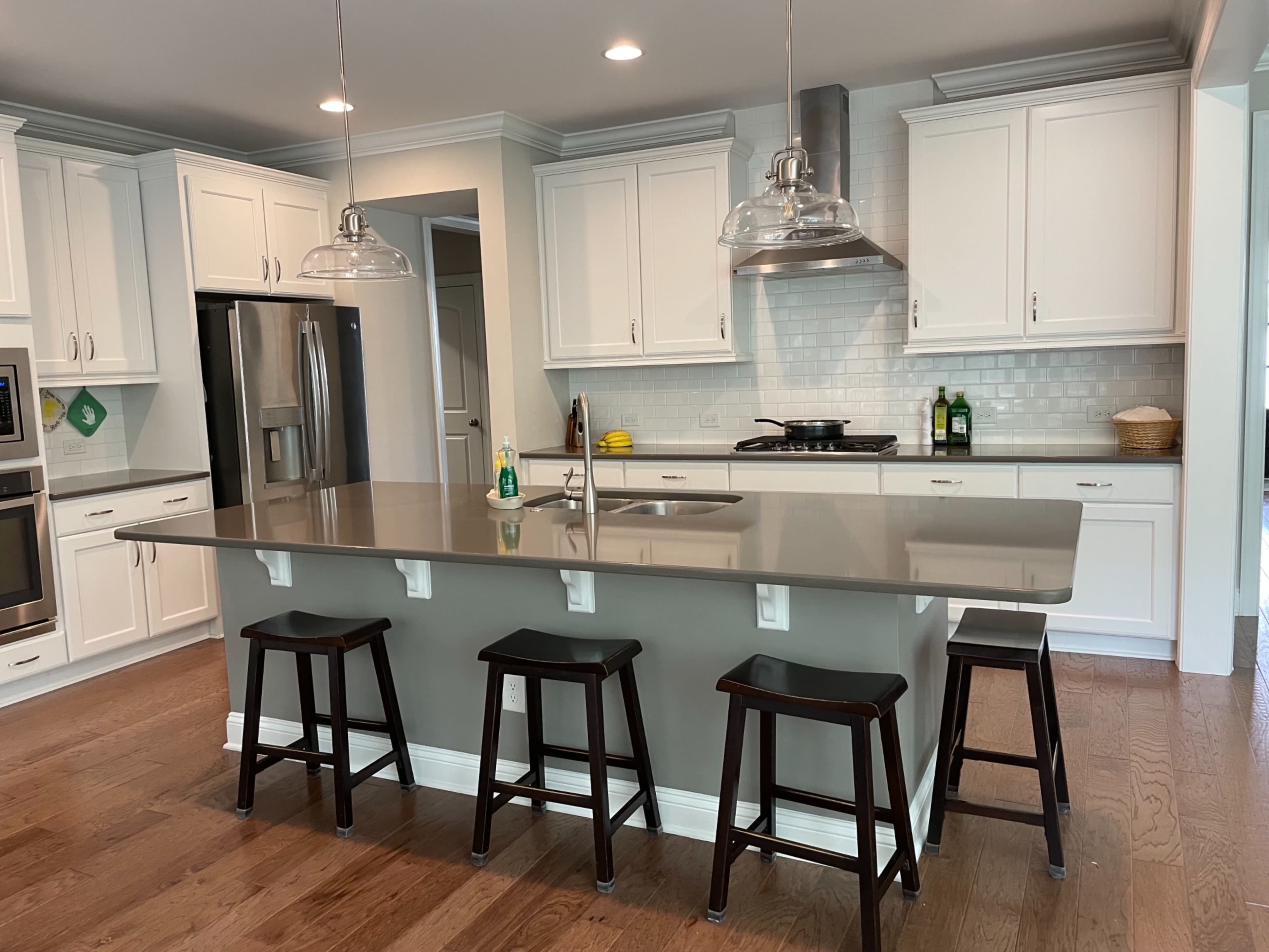 The kitchen features white cabinetry, a large island with bar stools, and stainless steel appliances.