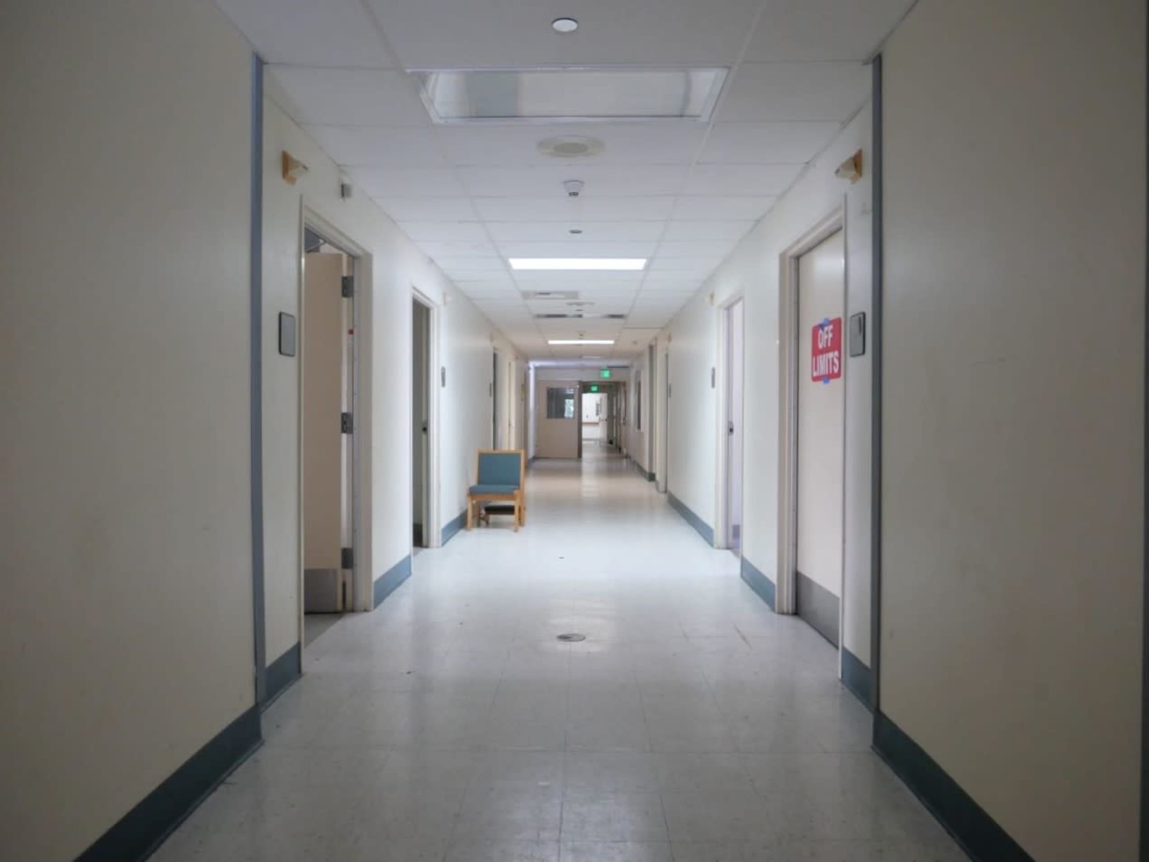 A long, empty hallway with closed doors on either side and a chair positioned against one wall.