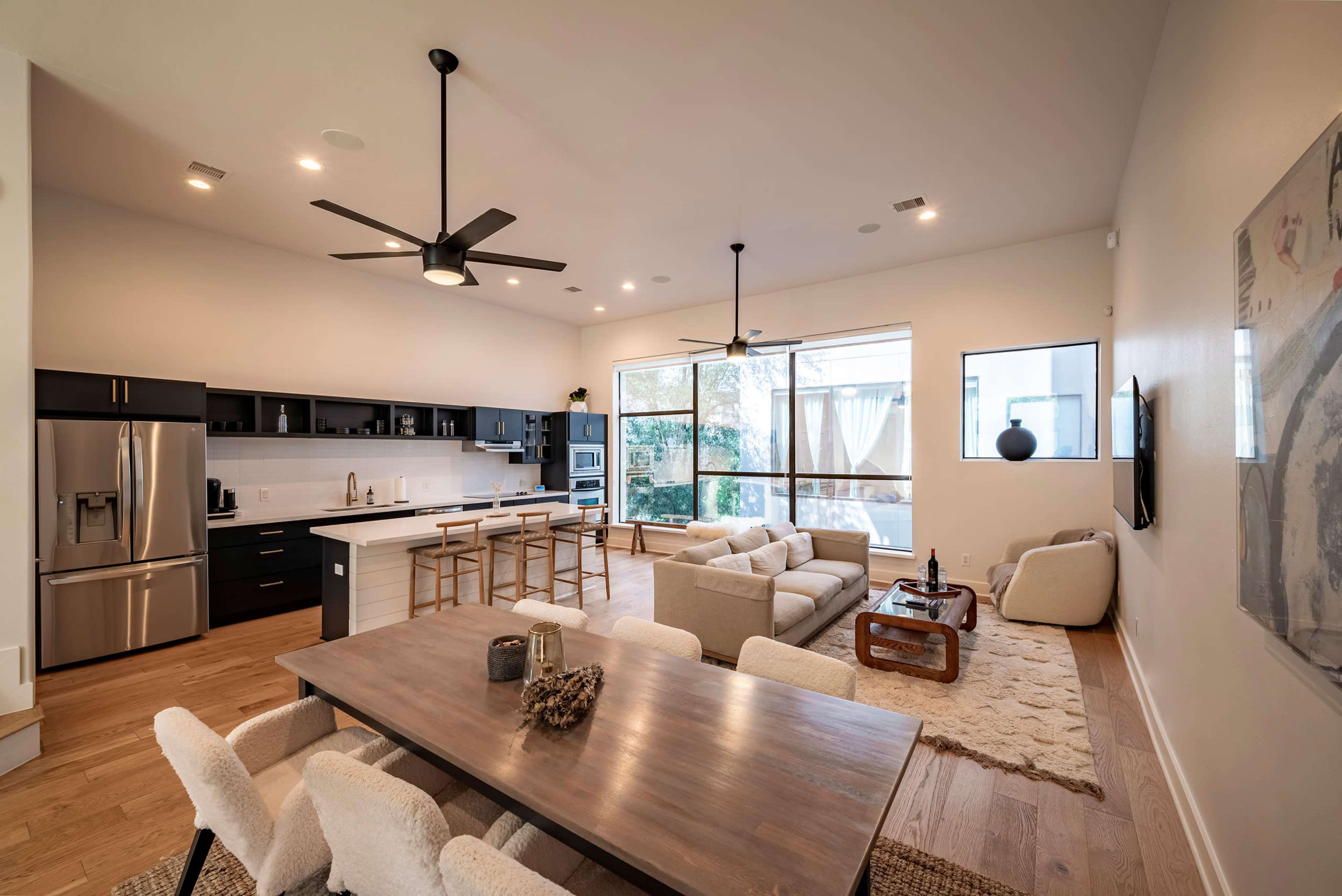 A modern open-concept living space with a kitchen, dining area, and seating arrangement by large windows.