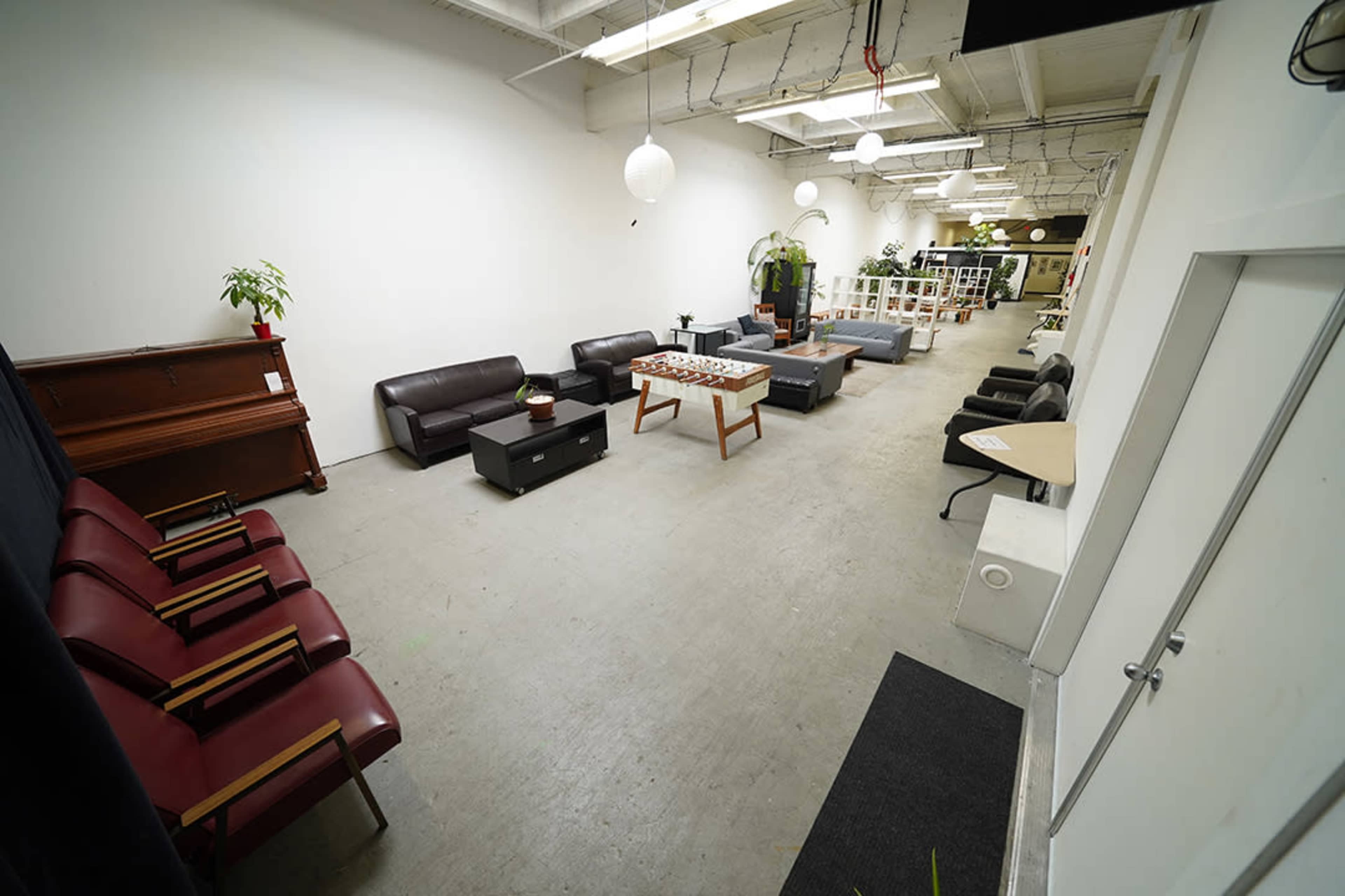 The image shows a spacious room with a mix of seating arrangements, including leather sofas, armchairs, and a coffee table, along with plants and decorative elements.