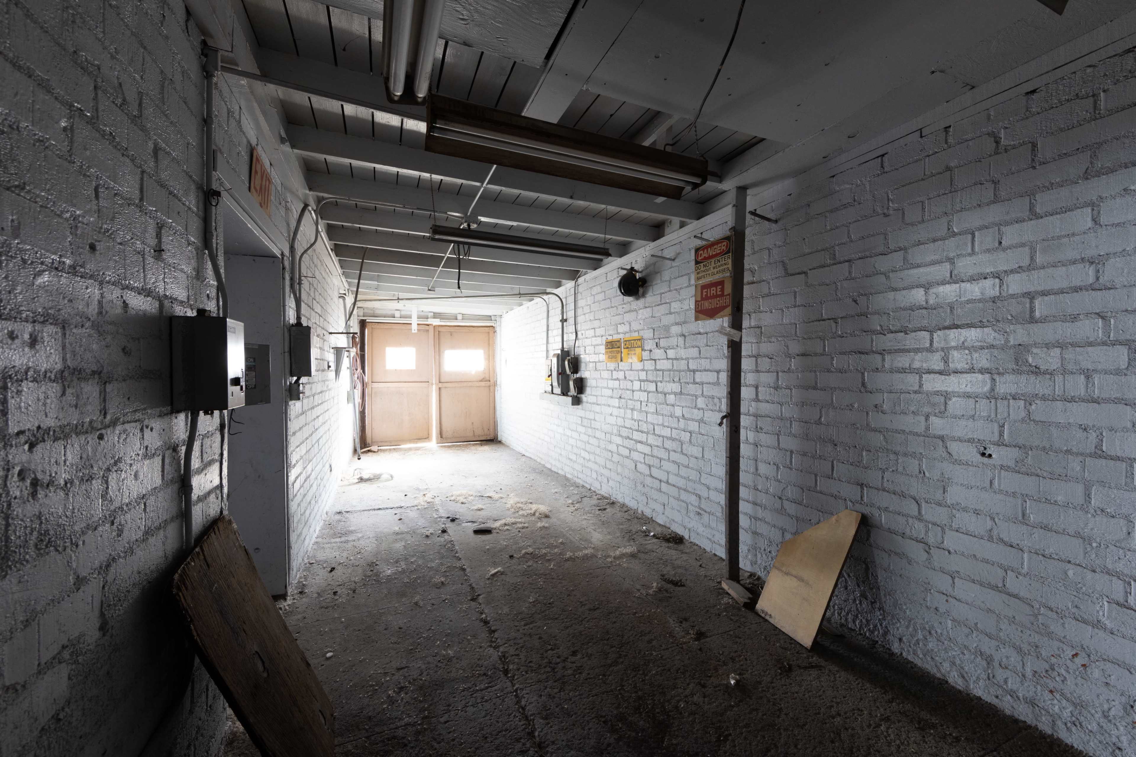 A dimly lit, abandoned corridor with concrete floors and white brick walls.