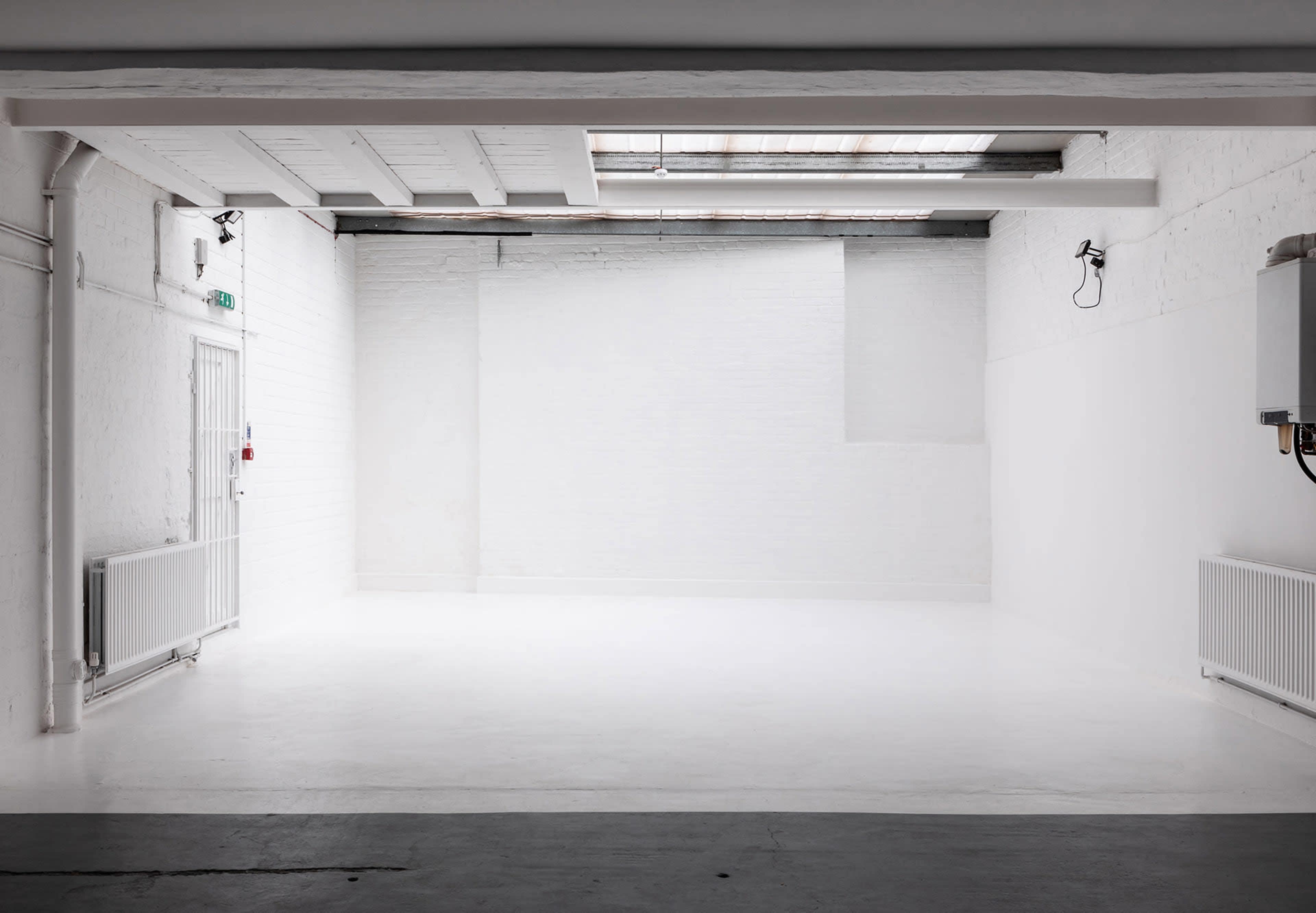 The image shows an empty, well-lit room with white walls and a concrete floor.