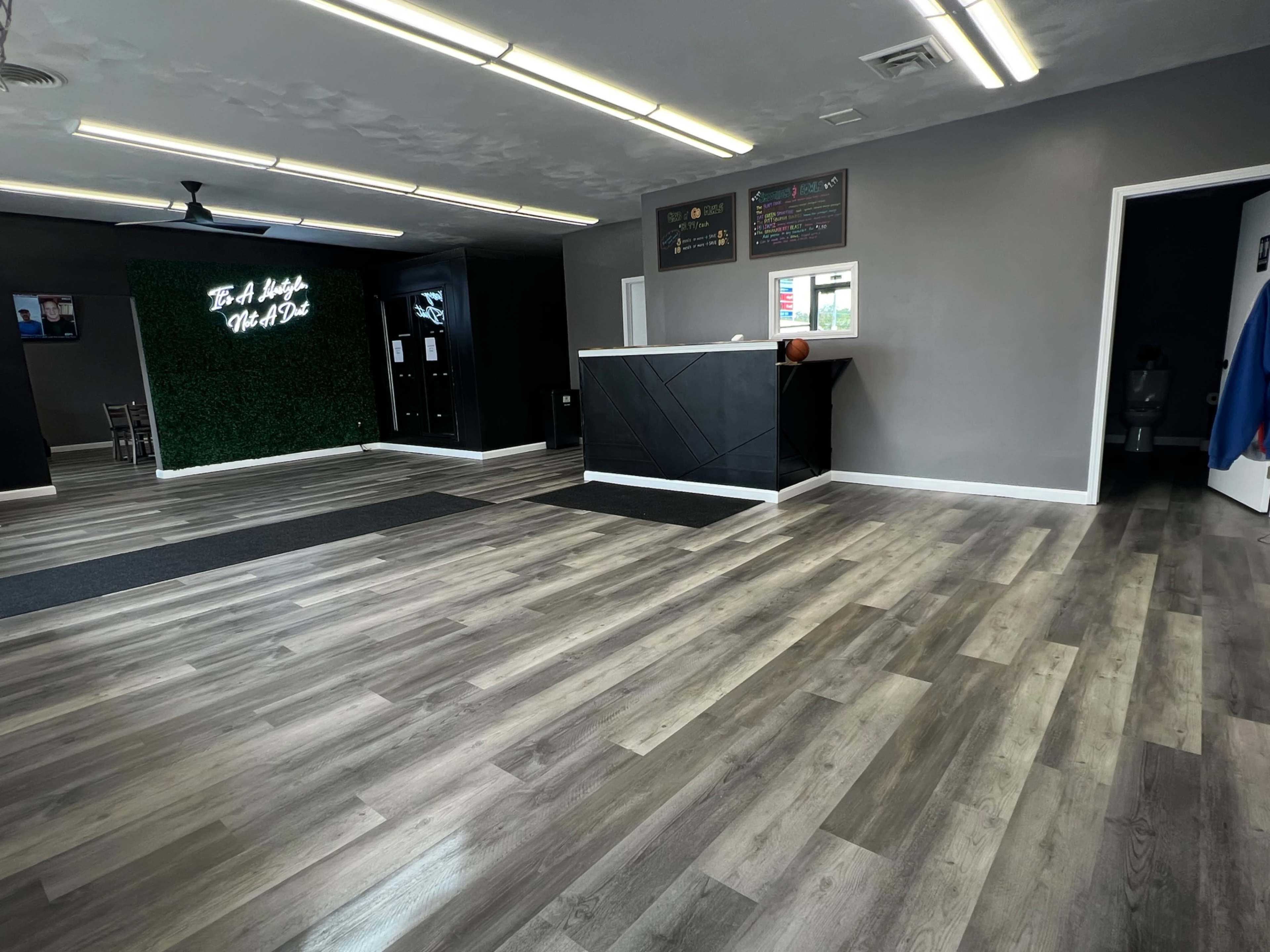 A modern interior space with wooden flooring, a reception counter, and a green accent wall with illuminated text.
