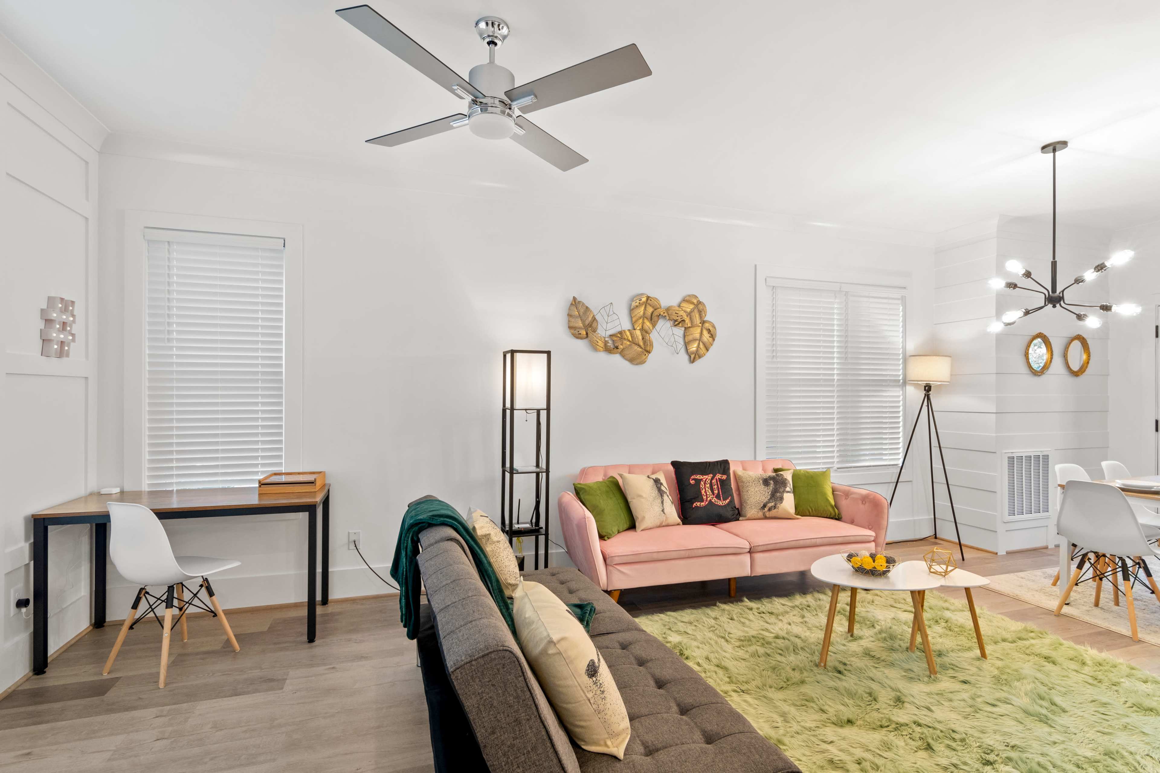 A modern living room with a pink sofa, a gray couch, a wooden table, and a green rug under a ceiling fan.