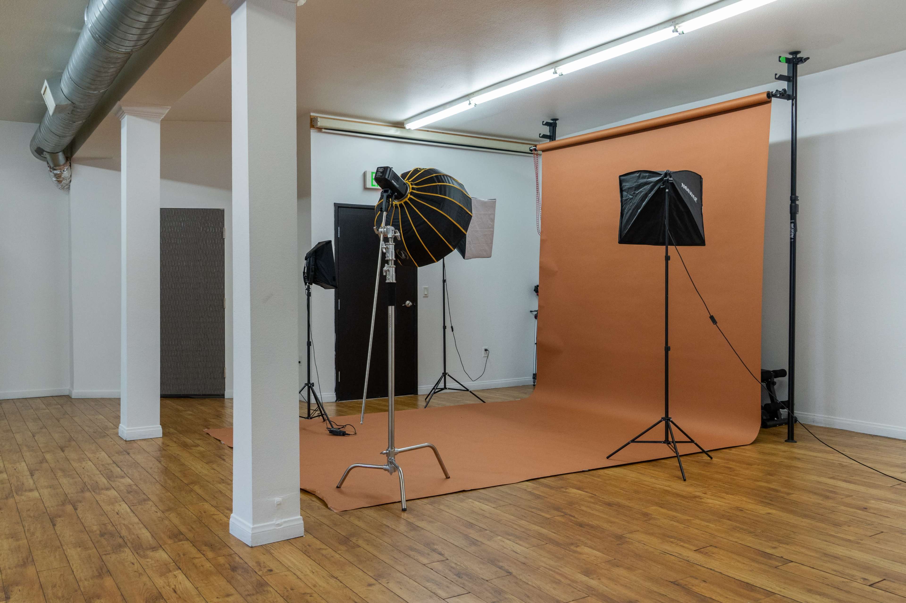 The image shows a photography studio with a brown backdrop, various lighting equipment, and wooden flooring.