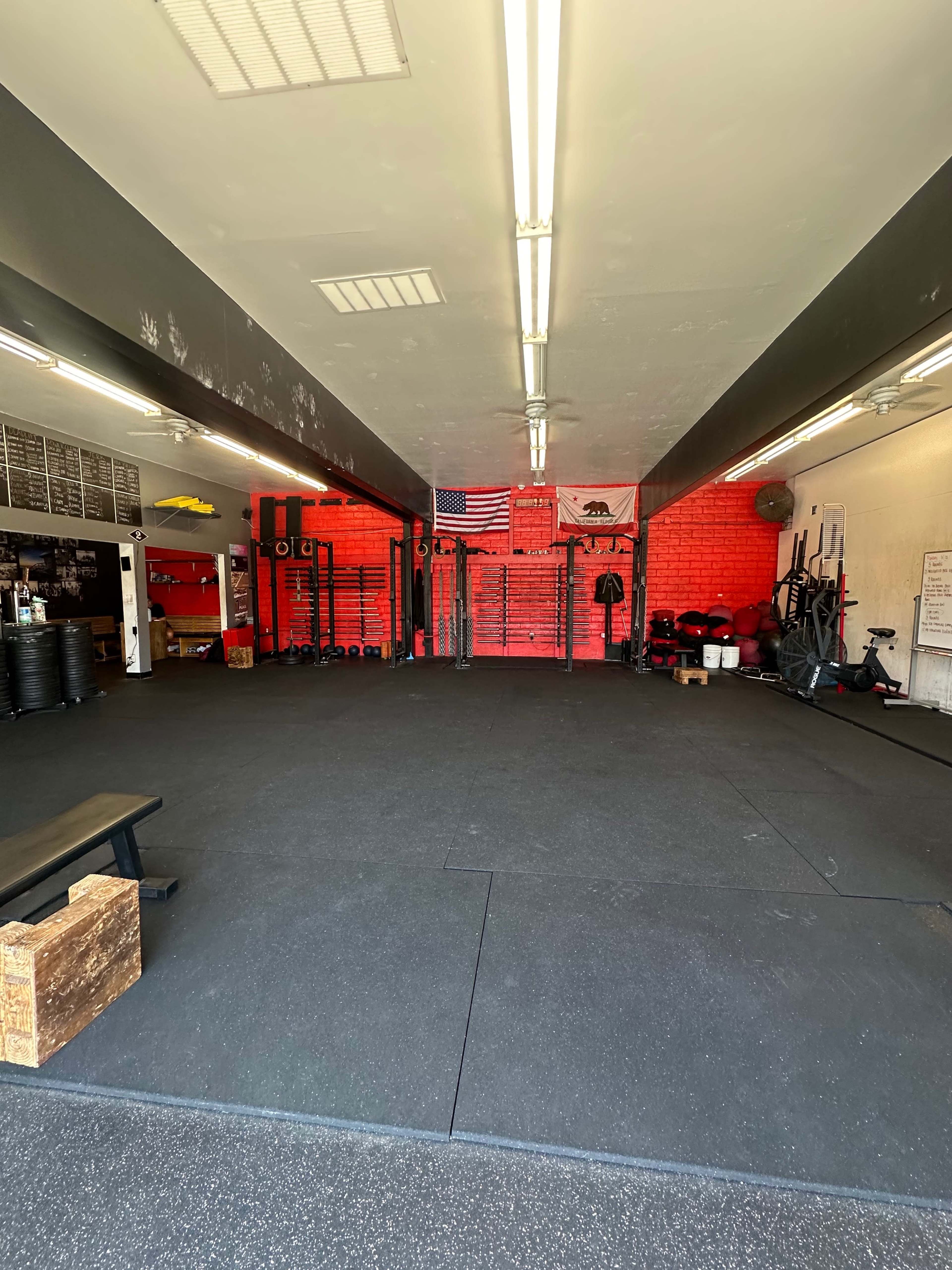 A fitness gym with rubber flooring, wall-mounted equipment, and an American flag displayed against a red wall.