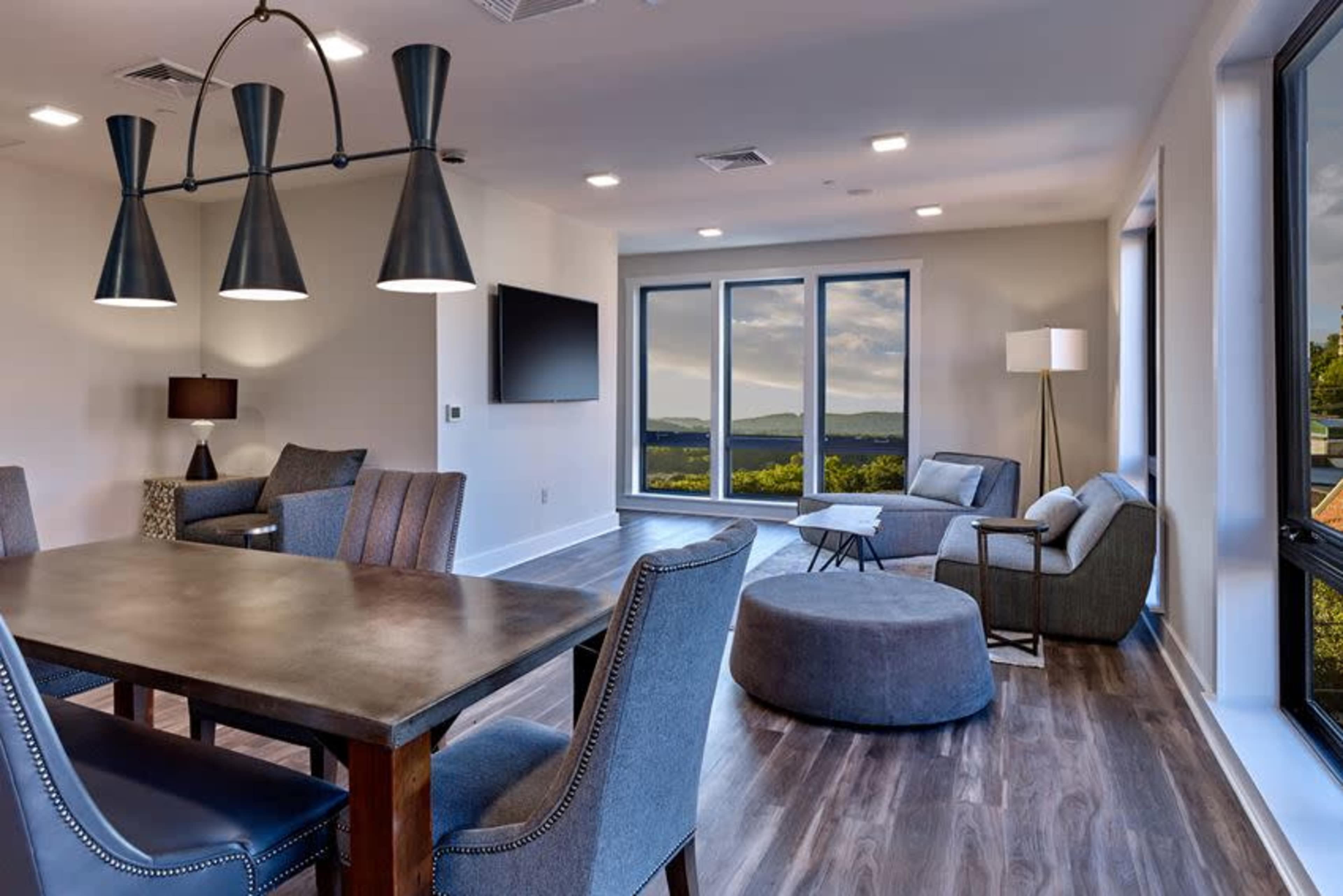 A modern living space features a dining table, lounge seating, and large windows showcasing a mountainous view.