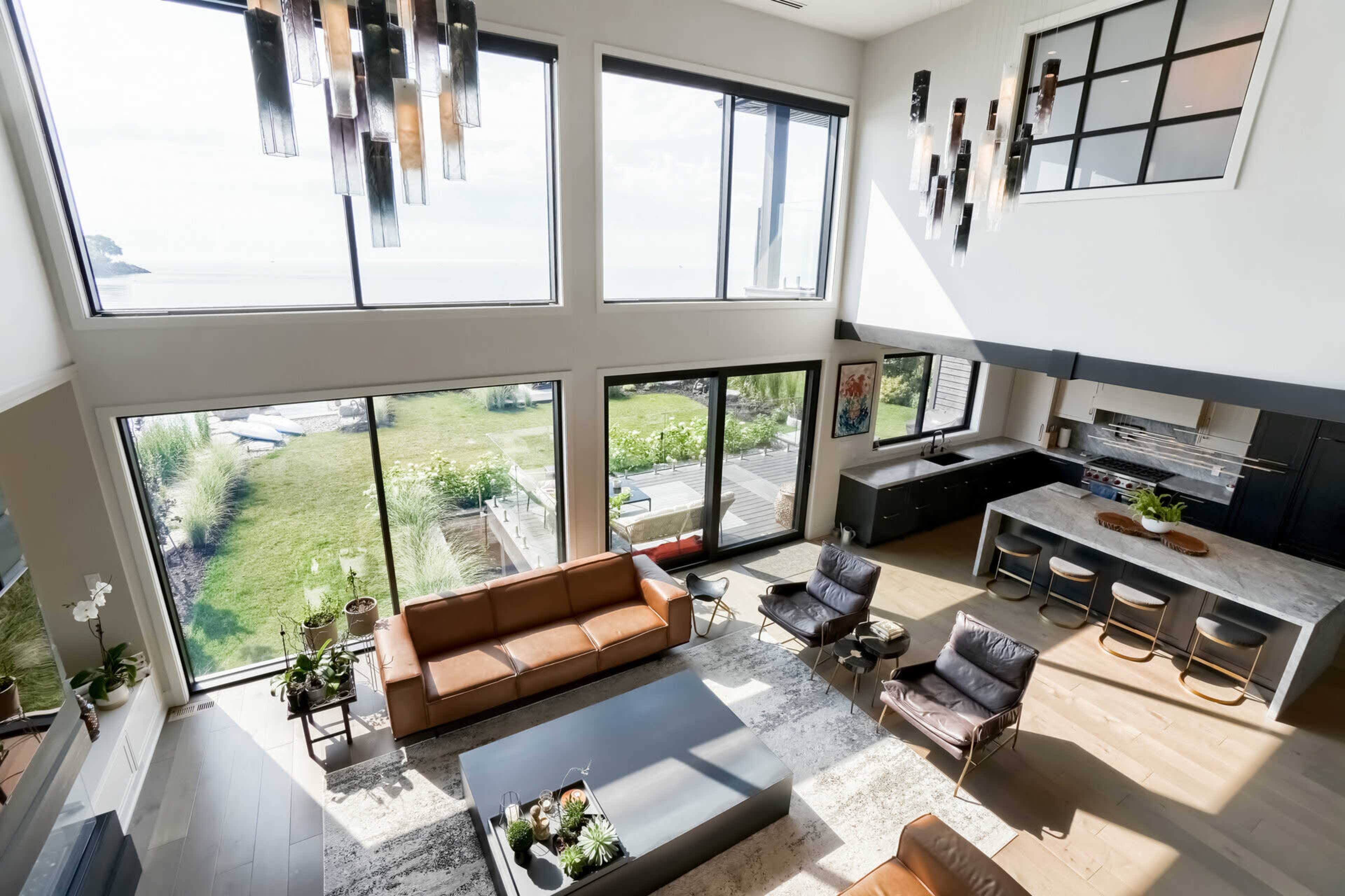 A spacious living room features large windows overlooking a grassy outdoor area, with modern furniture arranged around a central coffee table.